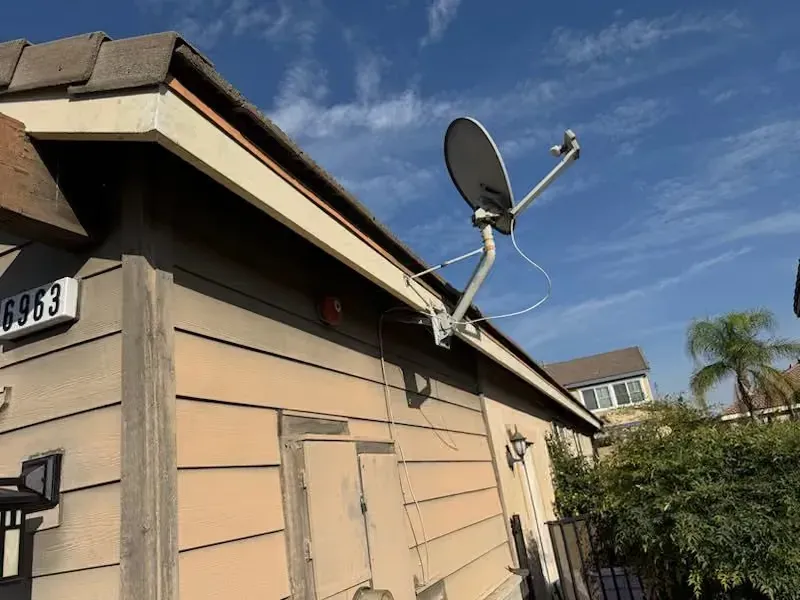 Tan house exterior with a roof-mounted satellite dish against a blue sky