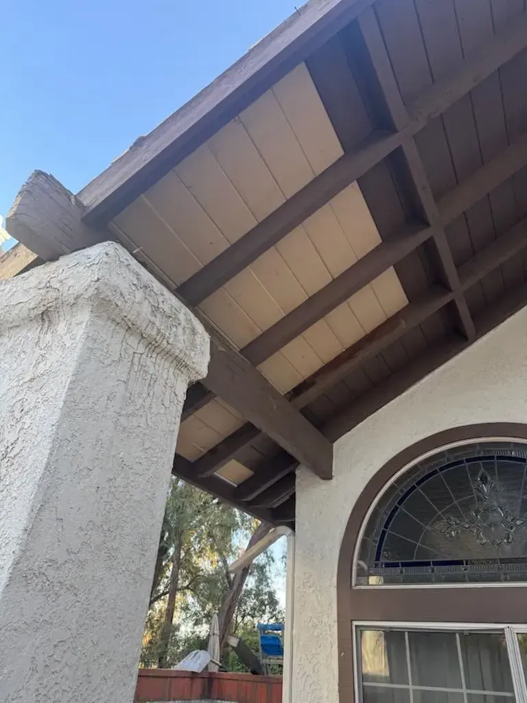 Exterior view of a house roof with exposed beams, a stucco column, and an arched window.
