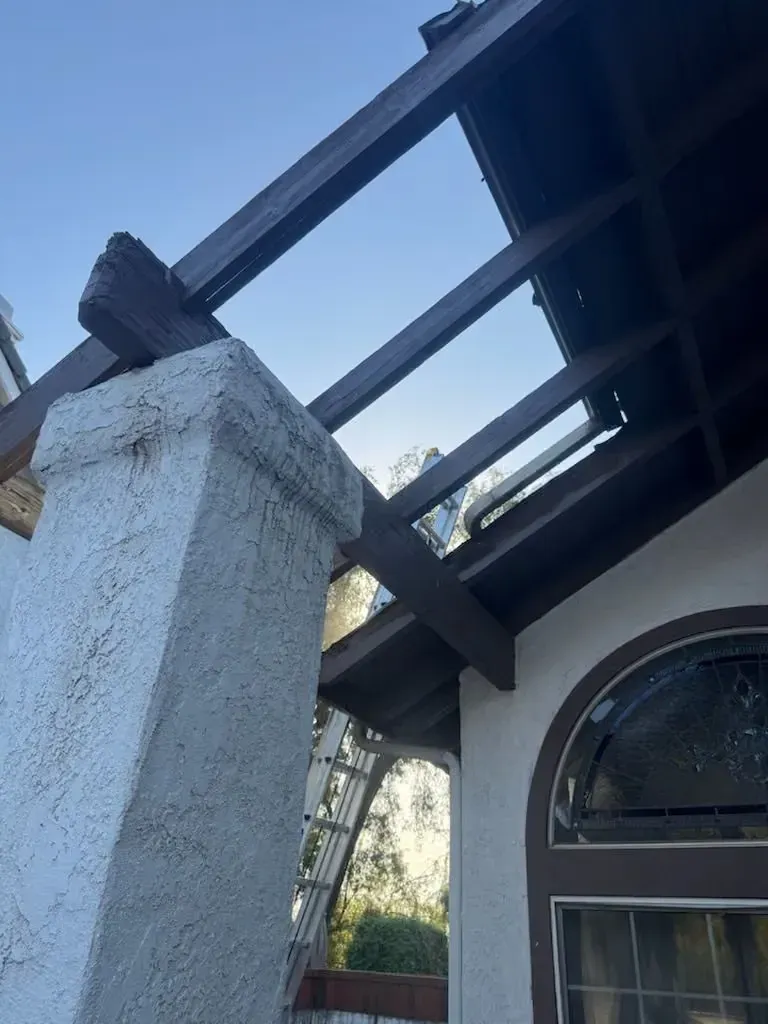 Damaged roof beams above a stucco pillar and arched window on a house exterior