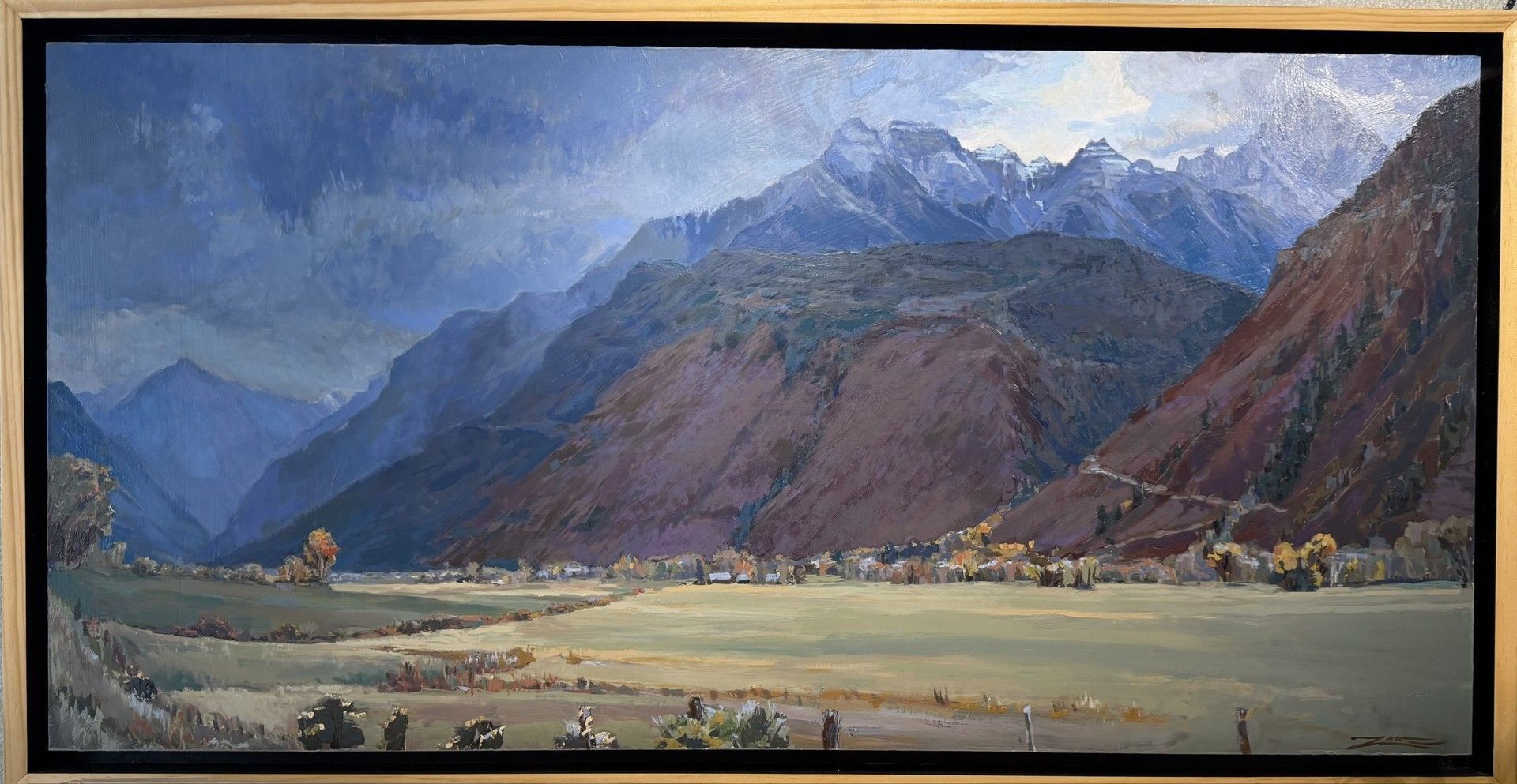 Framed mountain landscape with blue sky, green valley, and reddish cliffs
