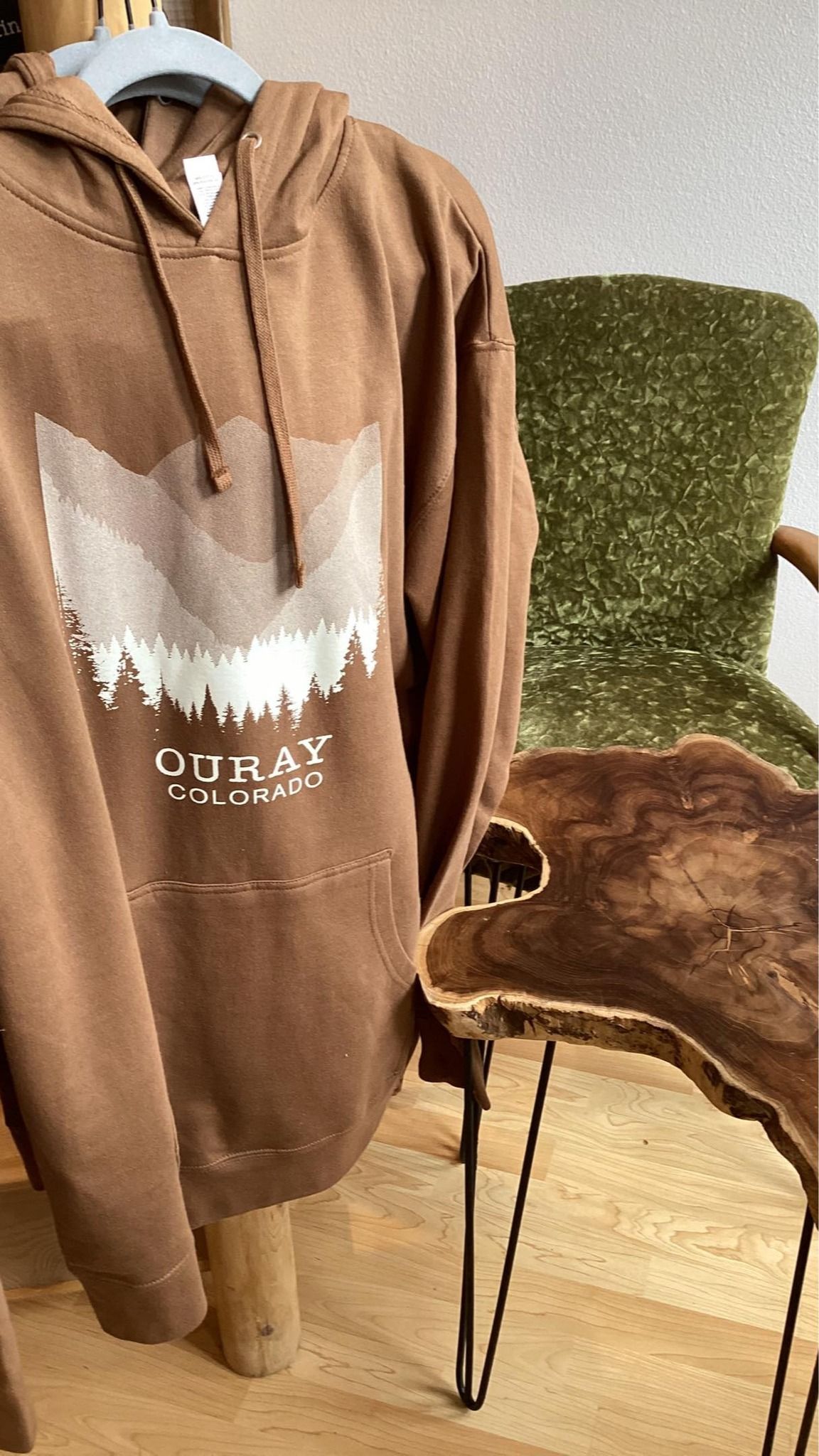 Brown hoodie on a hanger beside a green upholstered chair with a fur throw in a bright room
