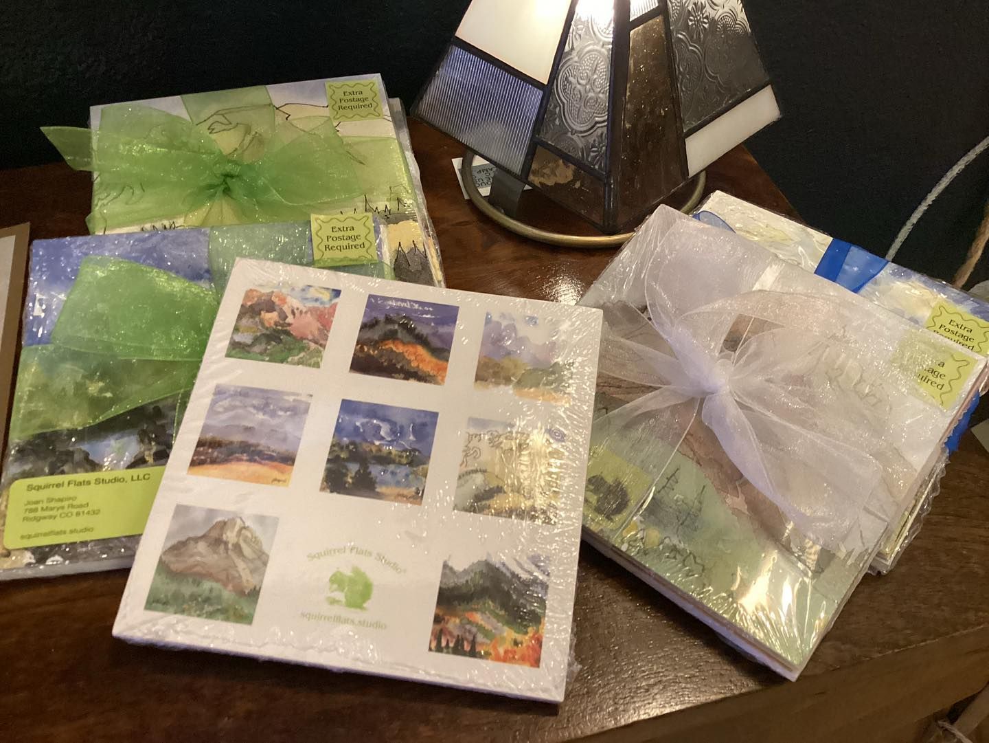 Gift-wrapped greeting cards and envelopes displayed on a table beside a decorative lamp.