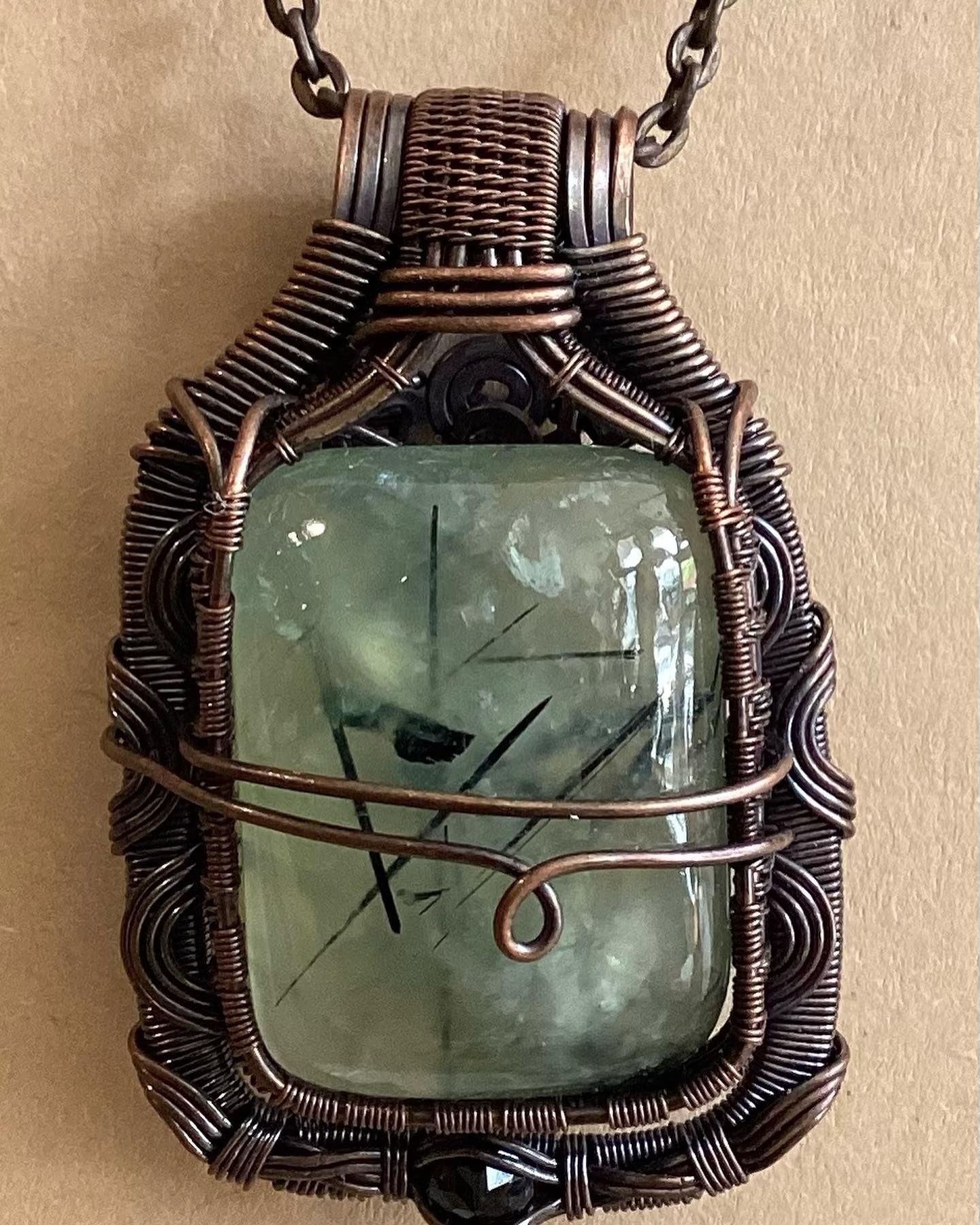 Wire-wrapped green stone pendant on a chain with copper and dark wire details