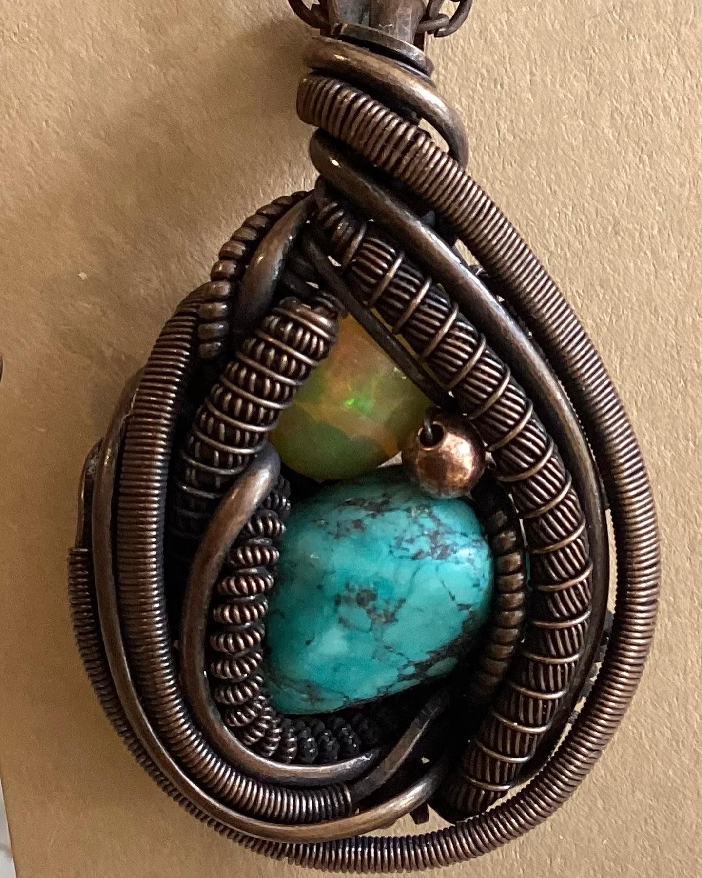 Wire-wrapped pendant with turquoise and green stones on a tan background