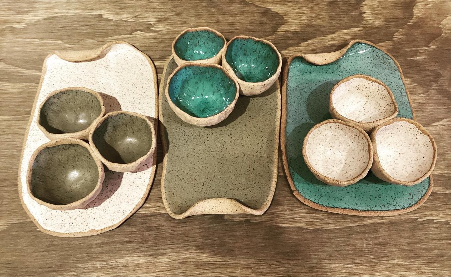 Three ceramic candle holders in cream, green, and teal on a wooden surface.