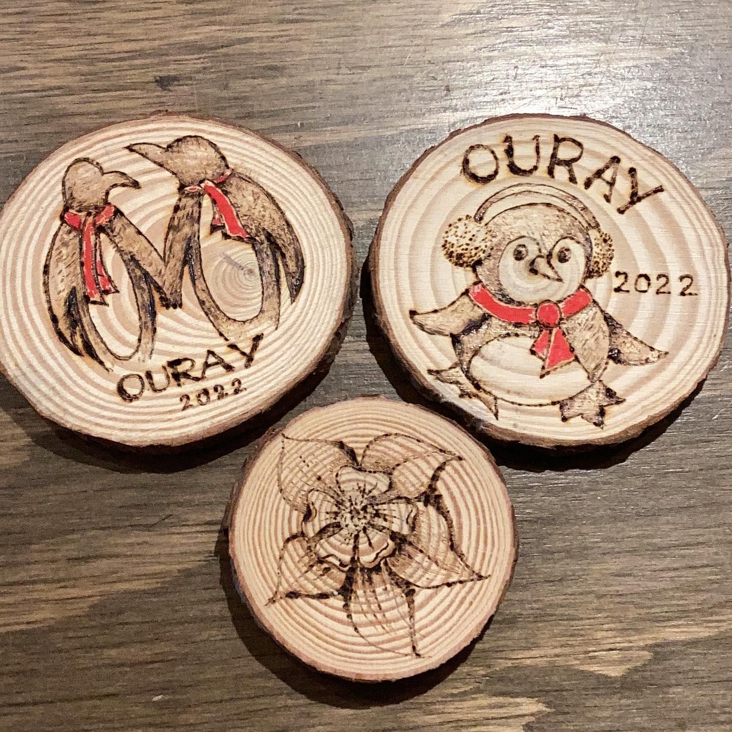 Three engraved wooden coasters: two with Quay 2022 designs and one floral design on a wood table.