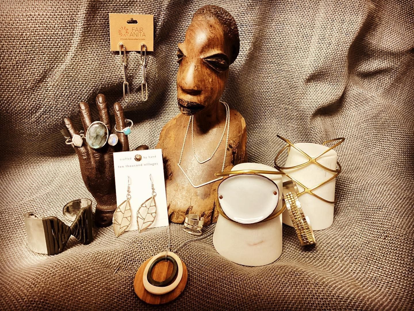 Still life of jewelry and a small sculpted bust on textured brown fabric, with white and gold objects.