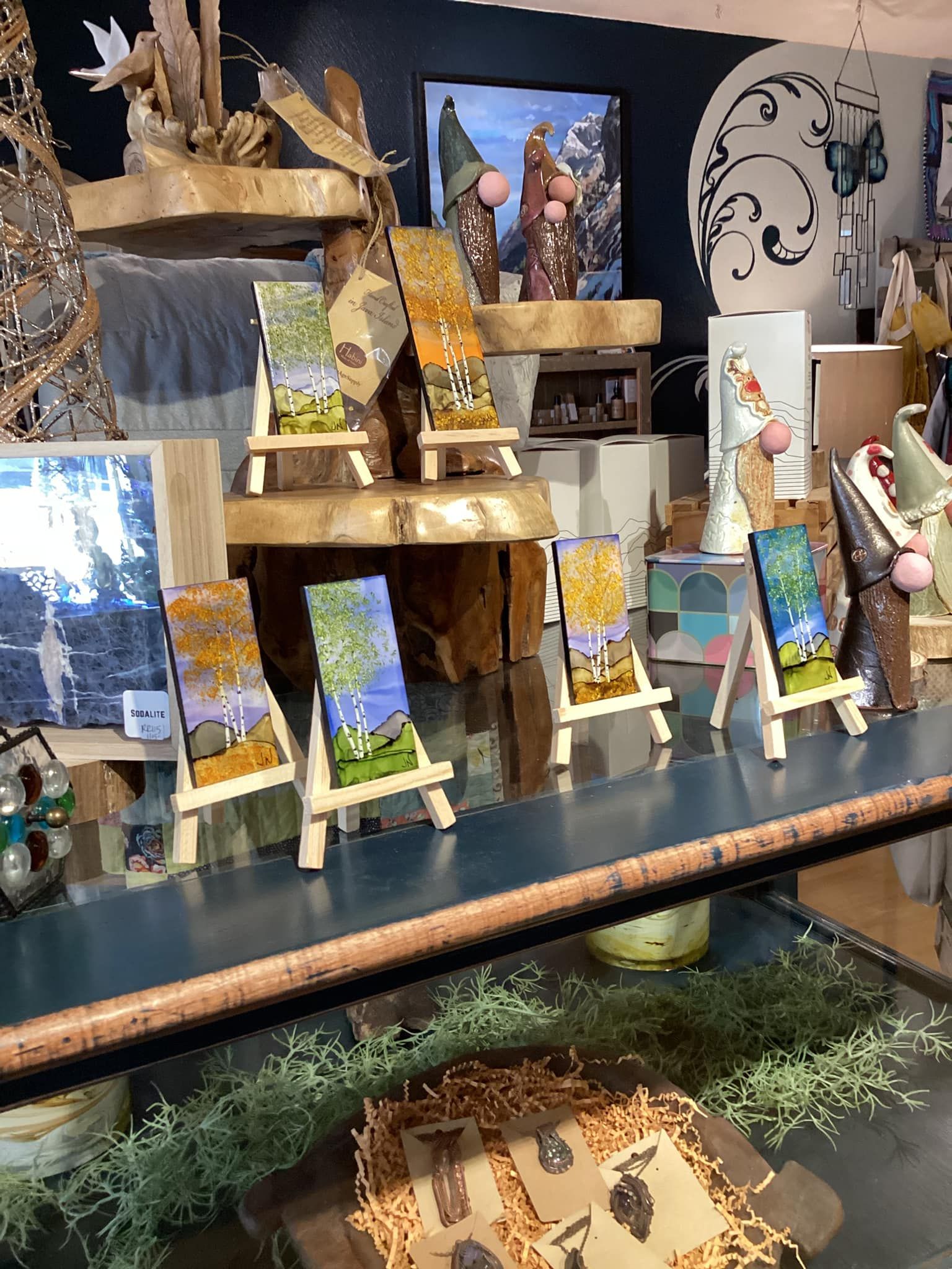 Display of colorful landscape art and small framed photos on tiered wooden shelves in a shop.