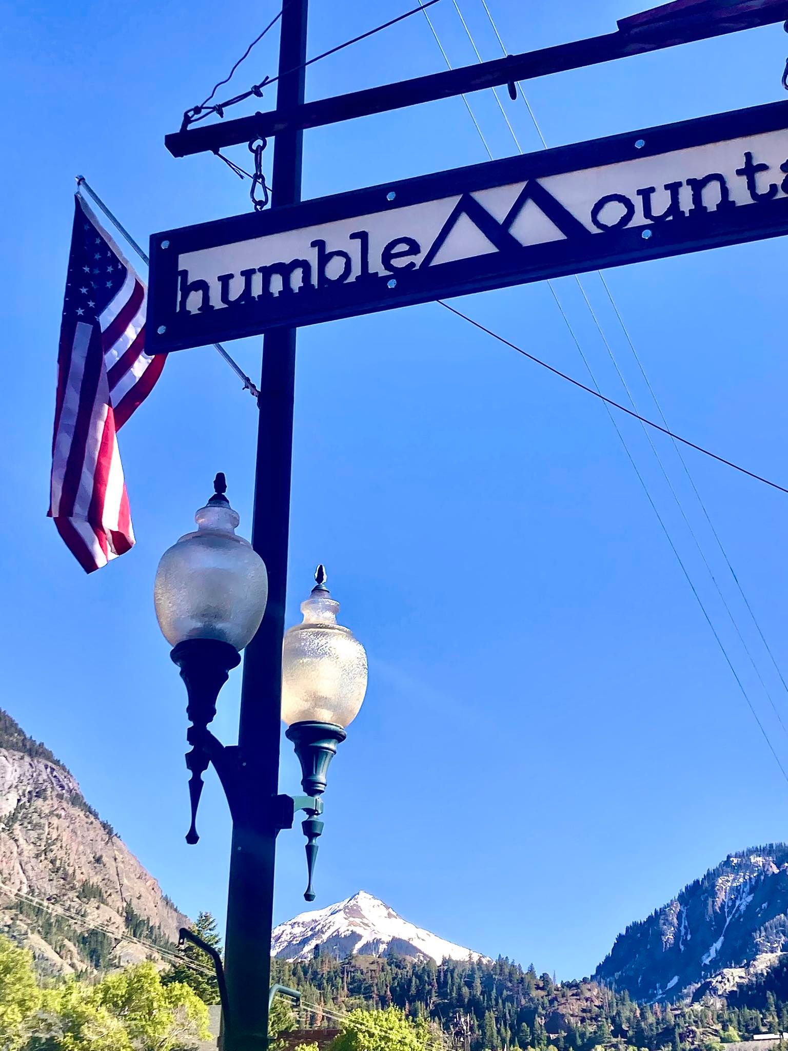 Street sign reading “humble” with an American flag, lamps, and mountains in the background