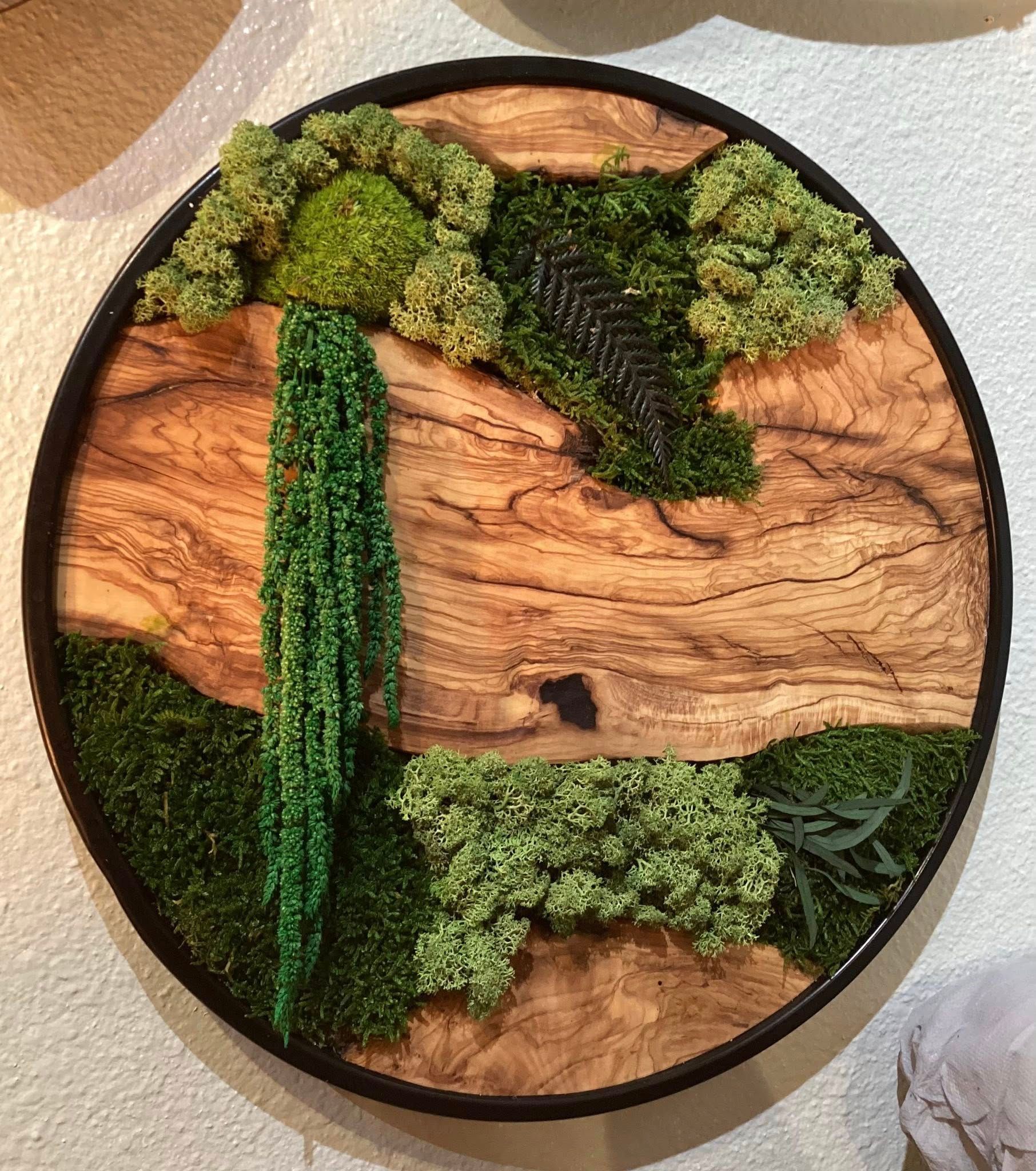 Circular wood art with green moss-like sections and a small dark center, resembling a tree or landscape