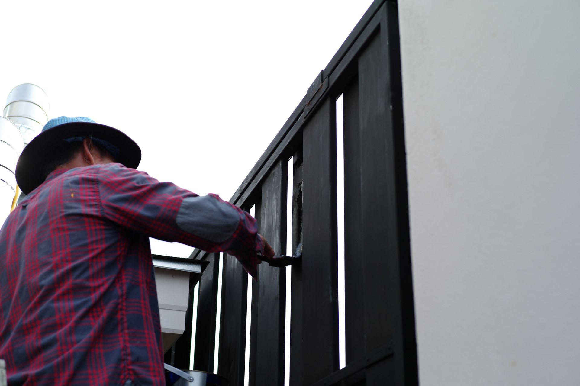 A man in a hat is painting a fence with a brush.