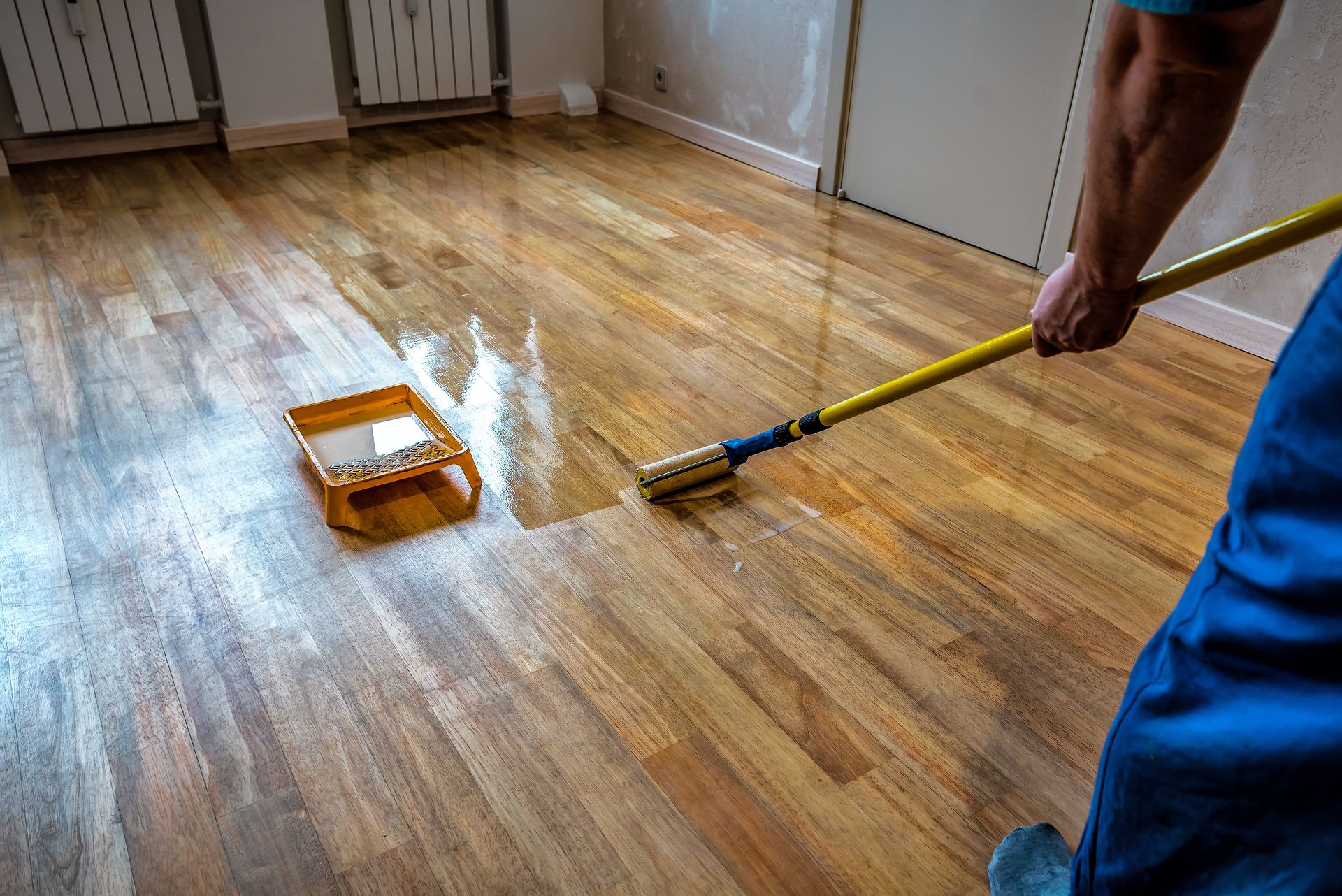 A man is painting a wooden floor with a roller.
