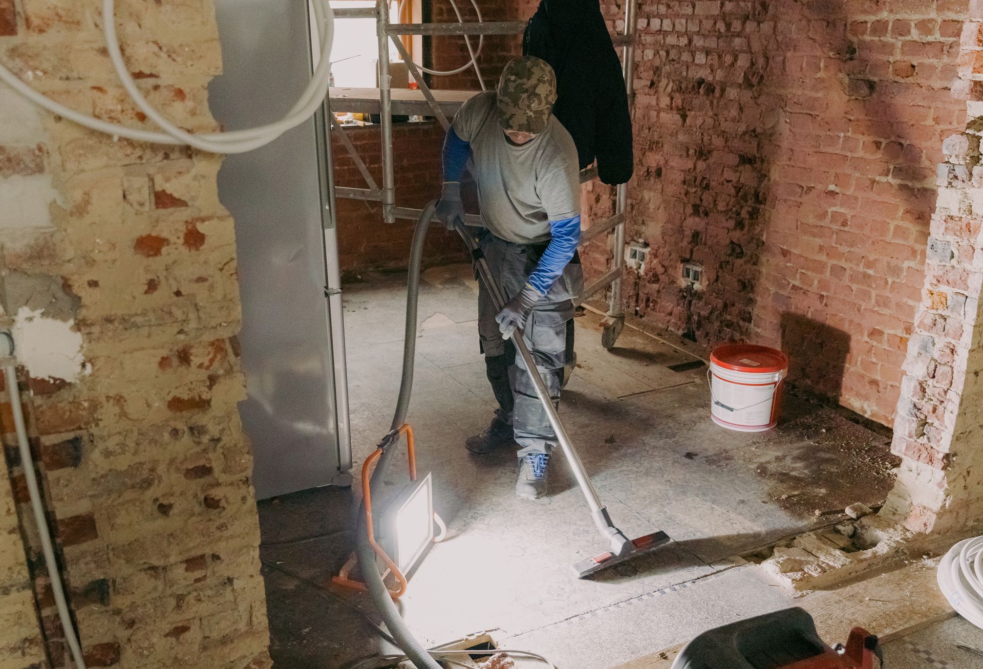 A man is using a vacuum cleaner in a room with brick walls.
