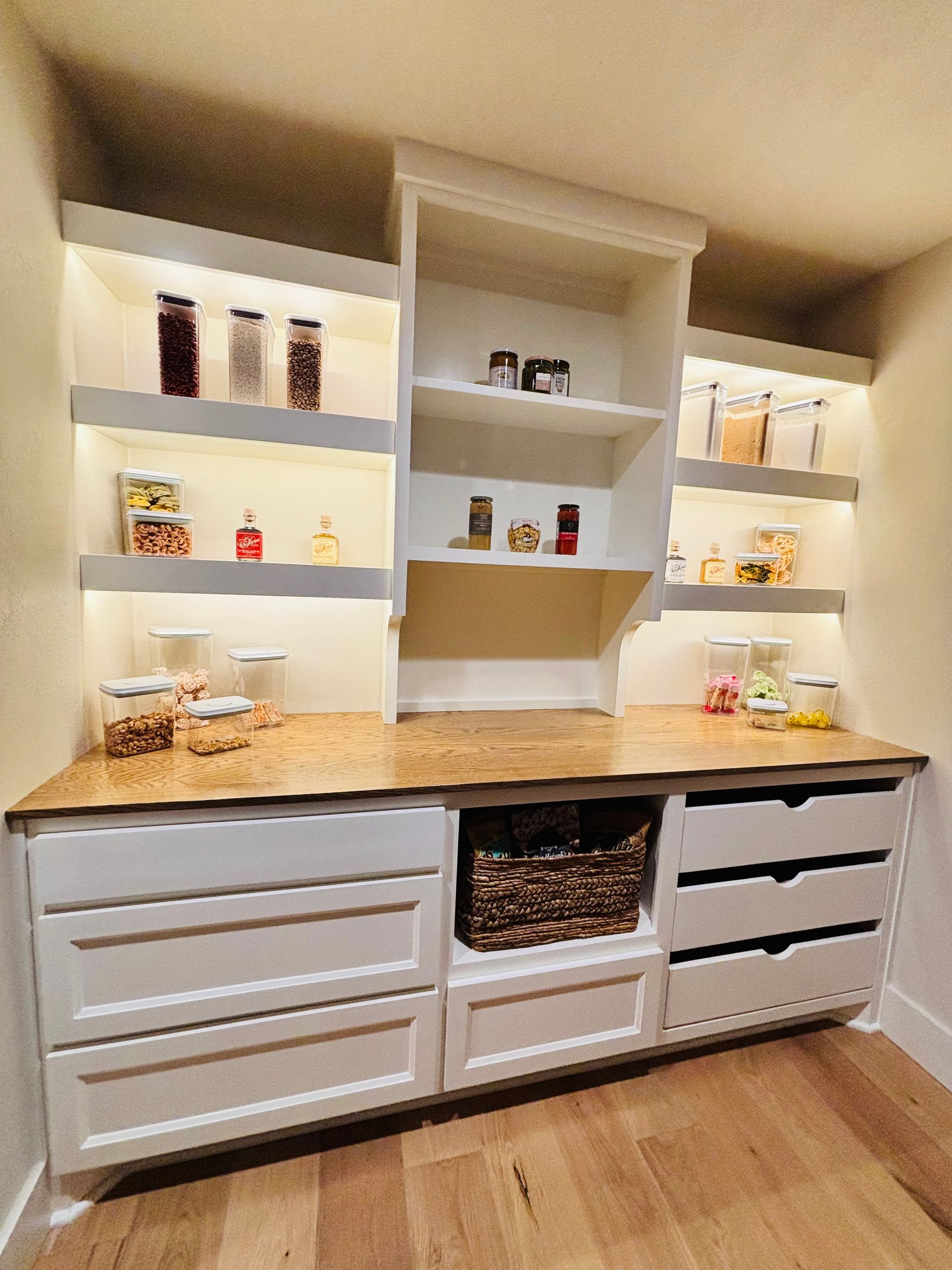 White built-in kitchen cabinets with lit shelves, granite countertop, and wood floor.
