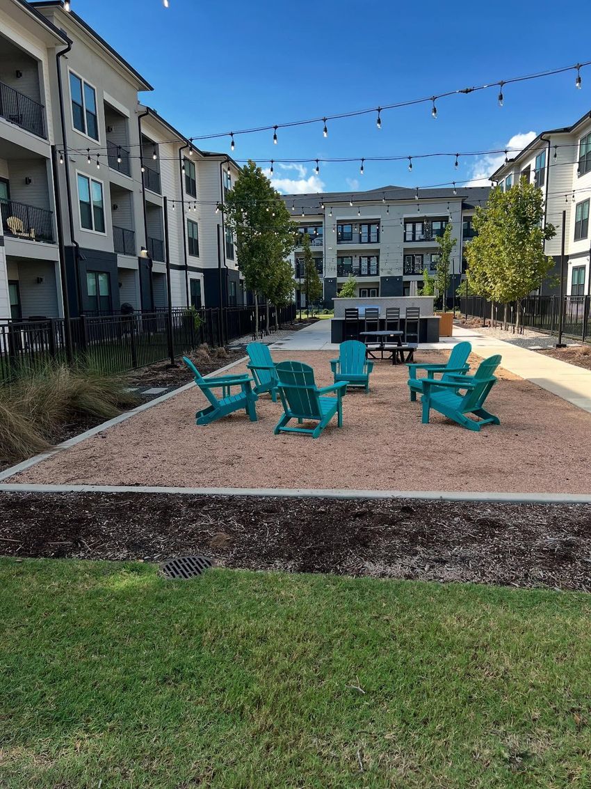 Outdoor seating area with teal chairs on gravel, between apartment buildings.