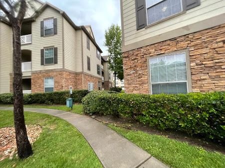 Apartment building courtyard with brick and beige siding, a sidewalk, and trimmed hedges on a cloudy day