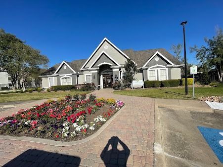 Landscaped residential clubhouse with flower bed, paved walkway, and clear blue sky