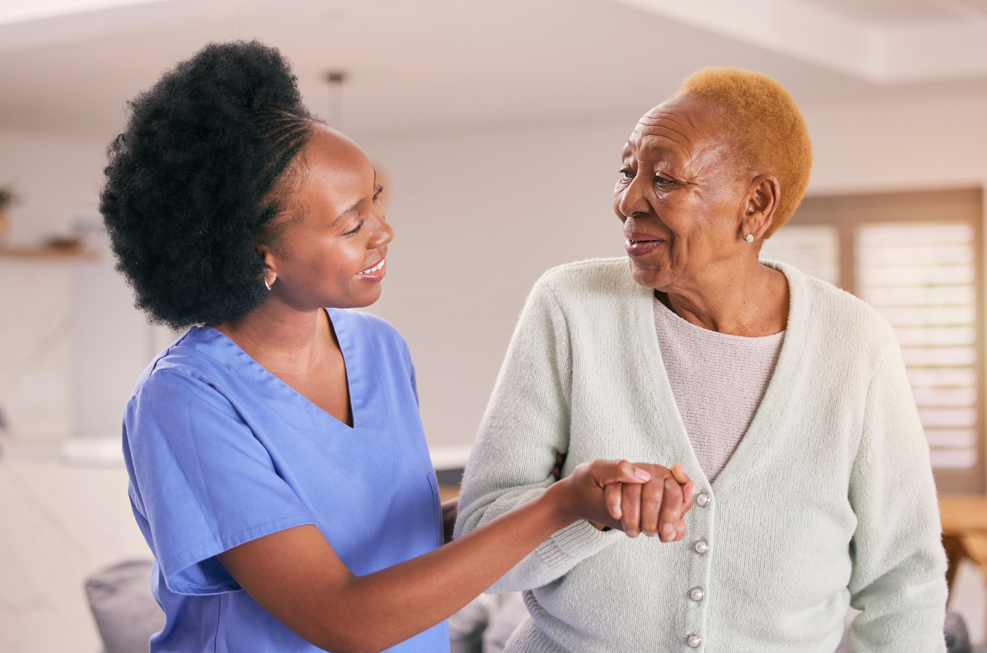 A nurse is helping an elderly woman walk by holding her hand.
