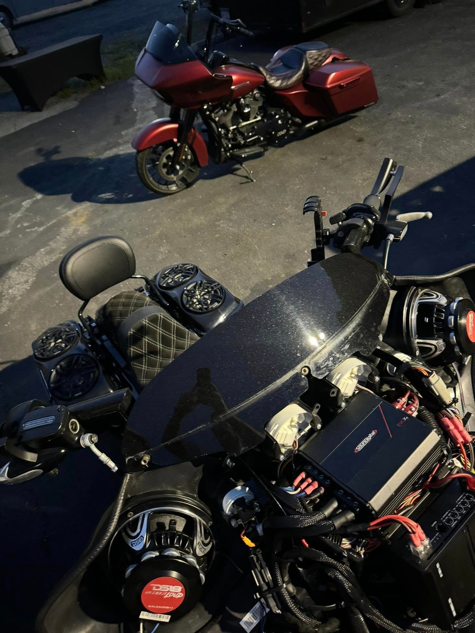 Two Harley-Davidson motorcycles, one black and one red, parked outdoors. Close-up on the black bike with audio components.