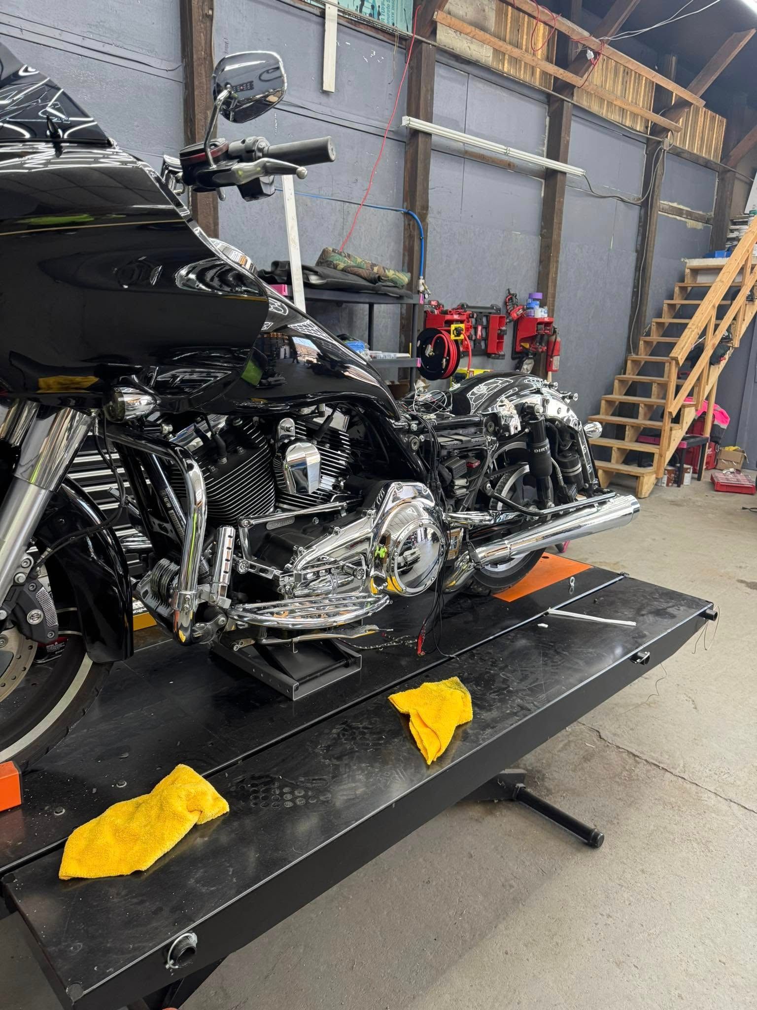 Black motorcycle on a lift in a workshop, with yellow cloths and wooden staircase.