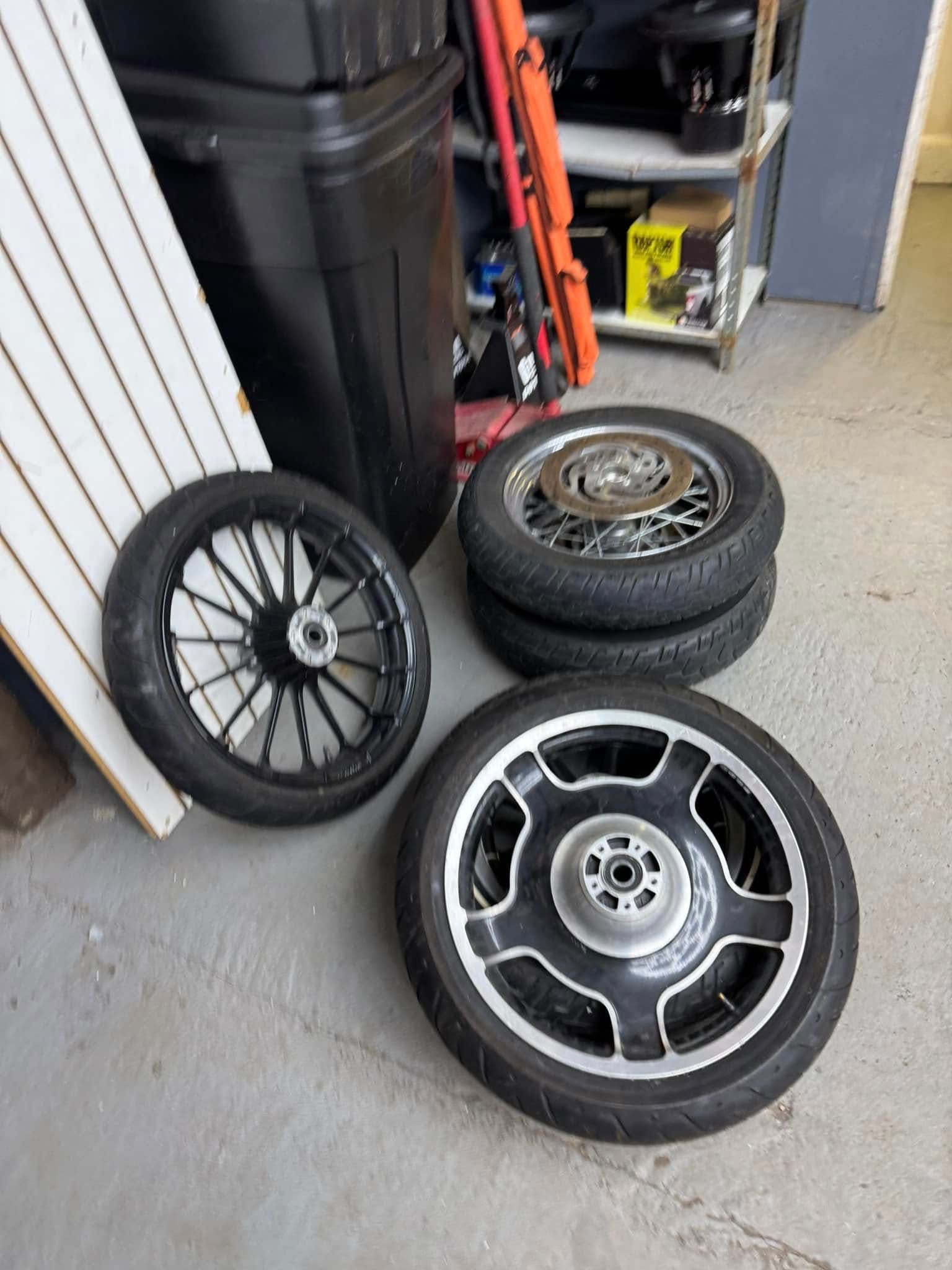 Motorcycle wheels stacked on a concrete floor near a black container and a shelf.