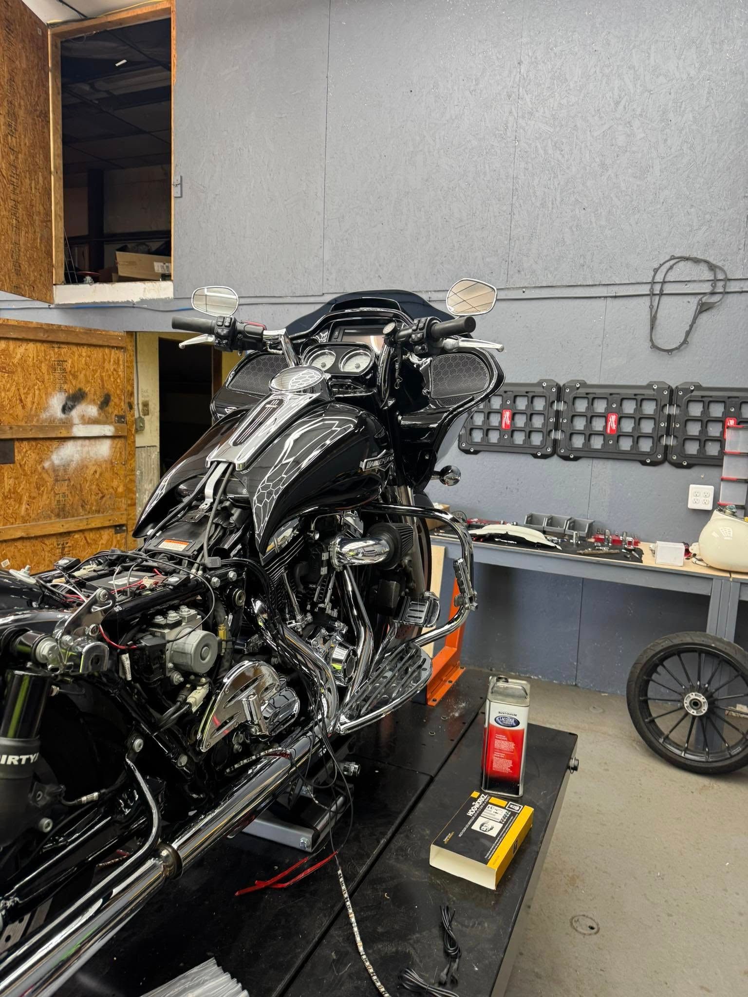 Black motorcycle, partially disassembled, in a garage. Chrome accents, tools, and parts on a table.