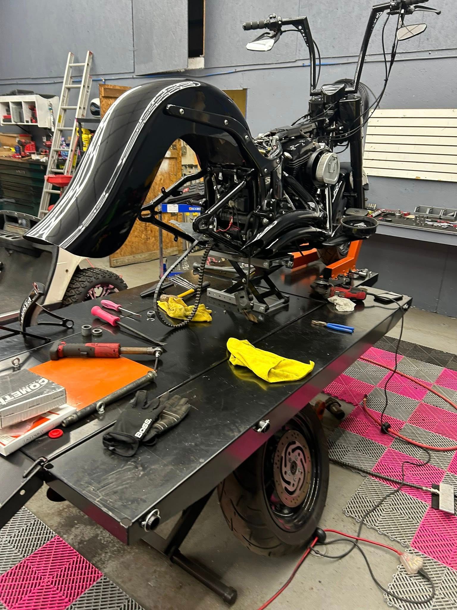 Black motorcycle on a lift in a workshop, under construction. Tools and parts are scattered around.
