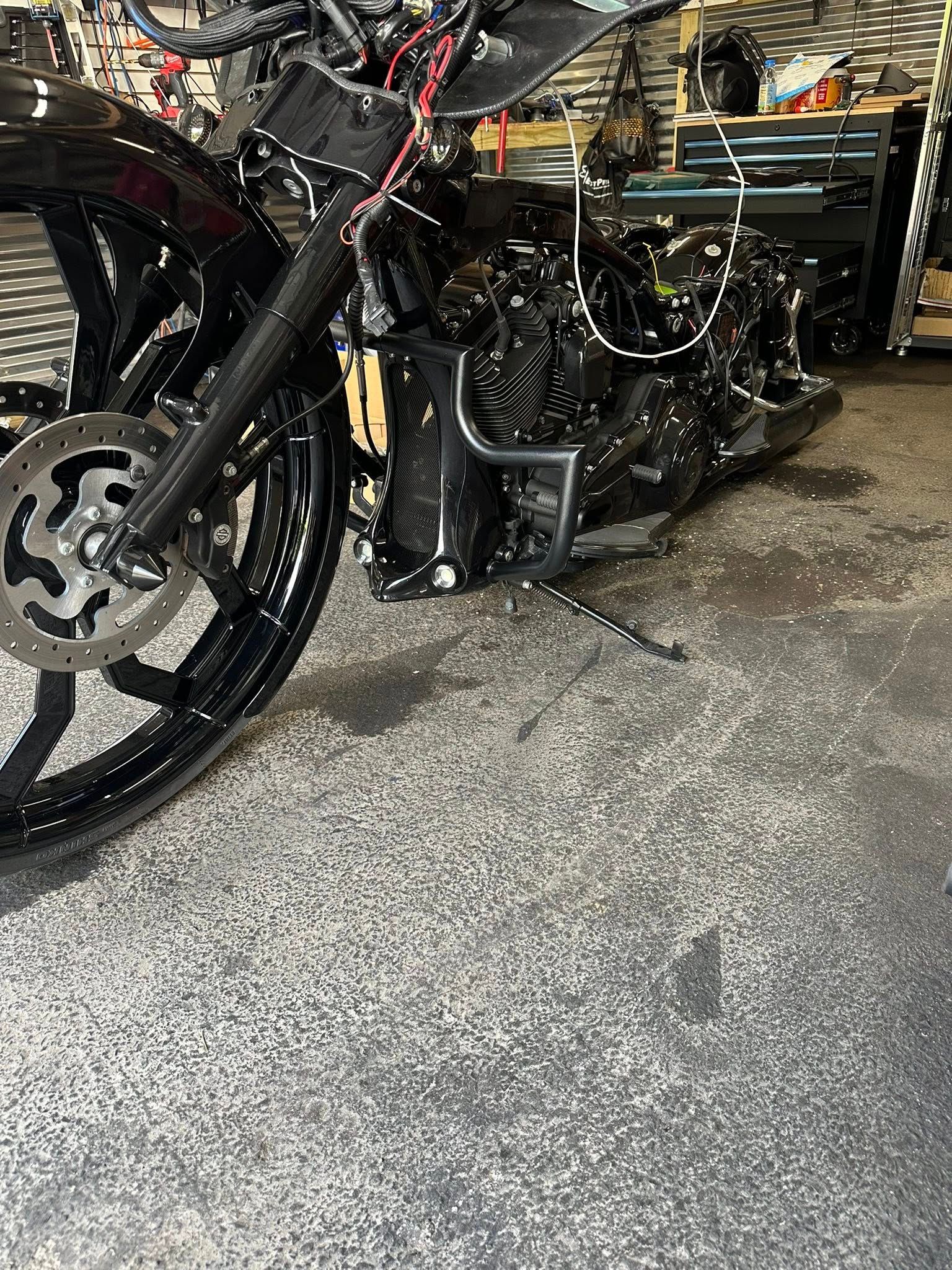 Black motorcycle being worked on in a garage; front wheel and components visible.