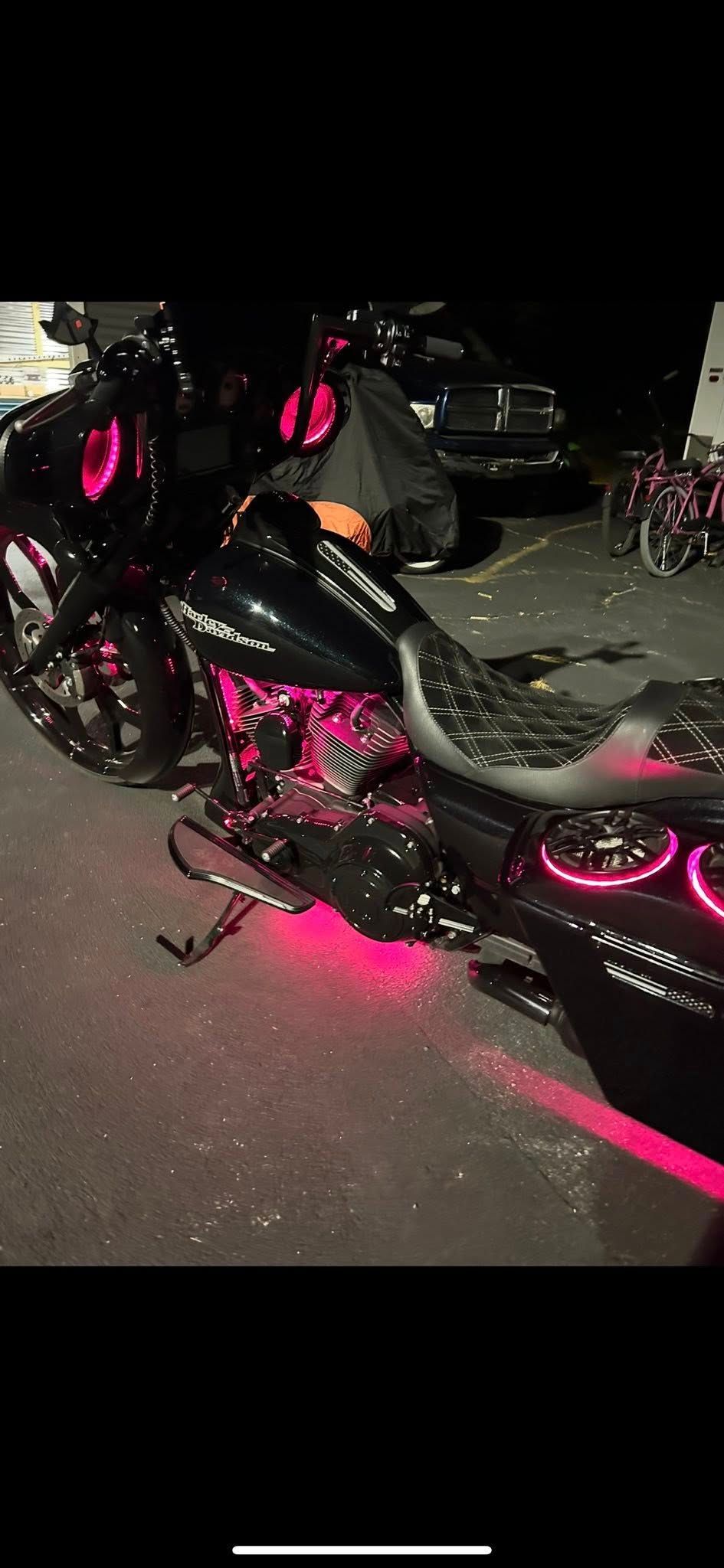 Black motorcycle with pink neon lights in a parking lot.