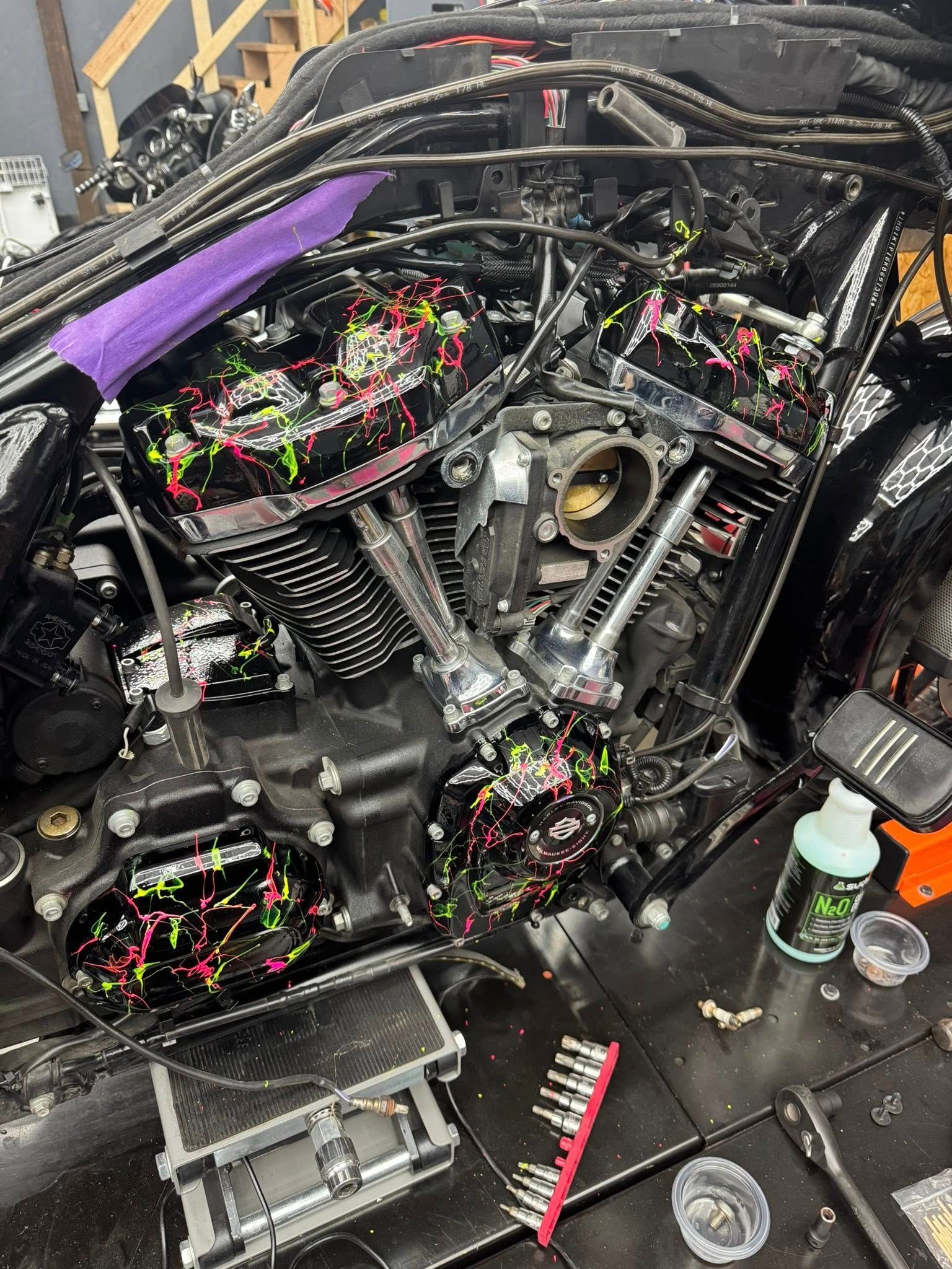 Motorcycle with splattered paint design being worked on, tools visible on a black surface.