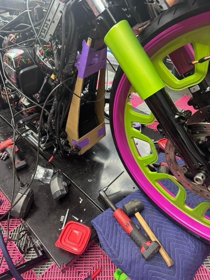Motorcycle being worked on, with bright pink and neon green accents. Tools on a blue cloth.