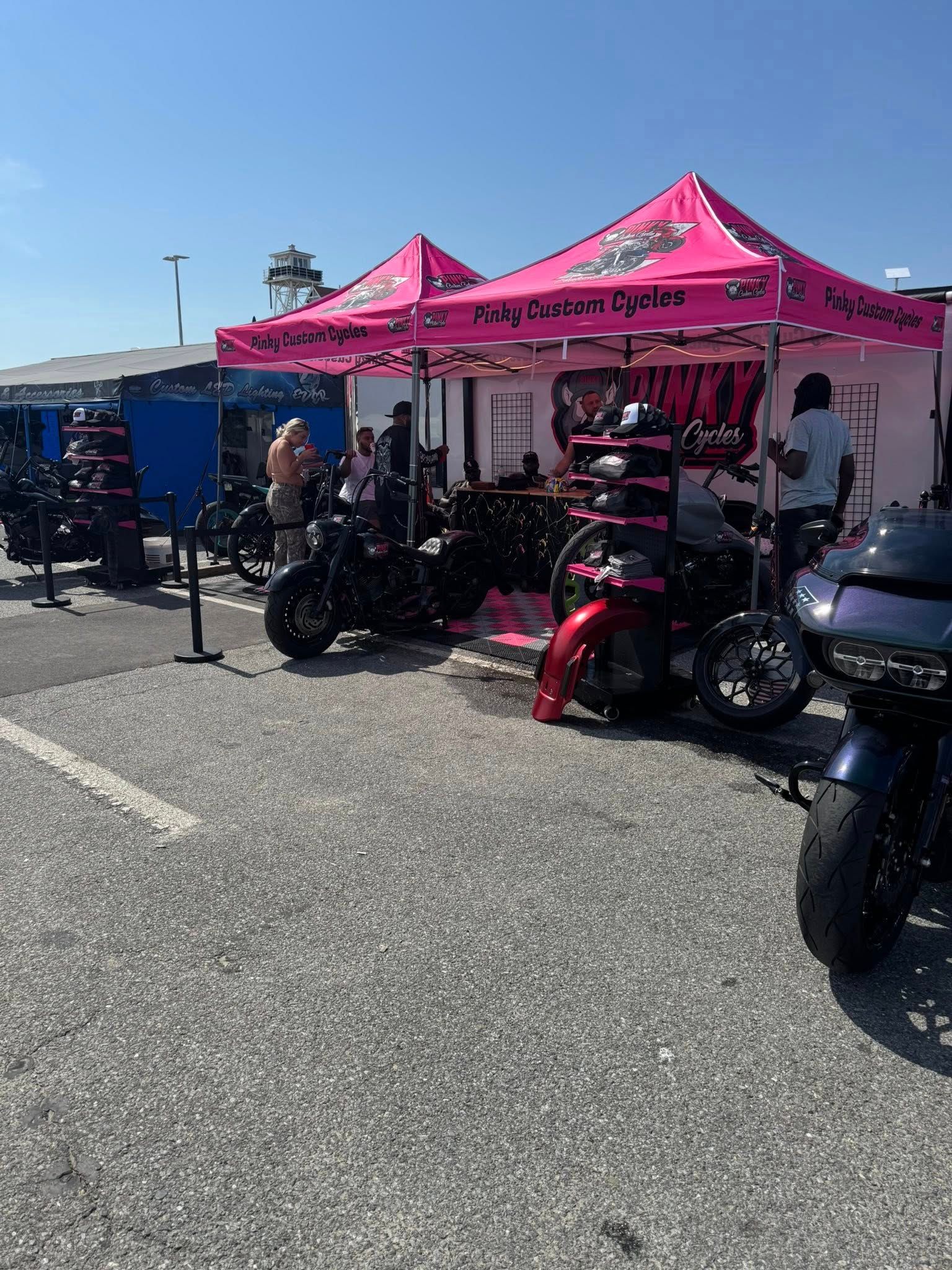 Motorcycle accessories booth with pink canopies, bikes parked outside, sunny day.