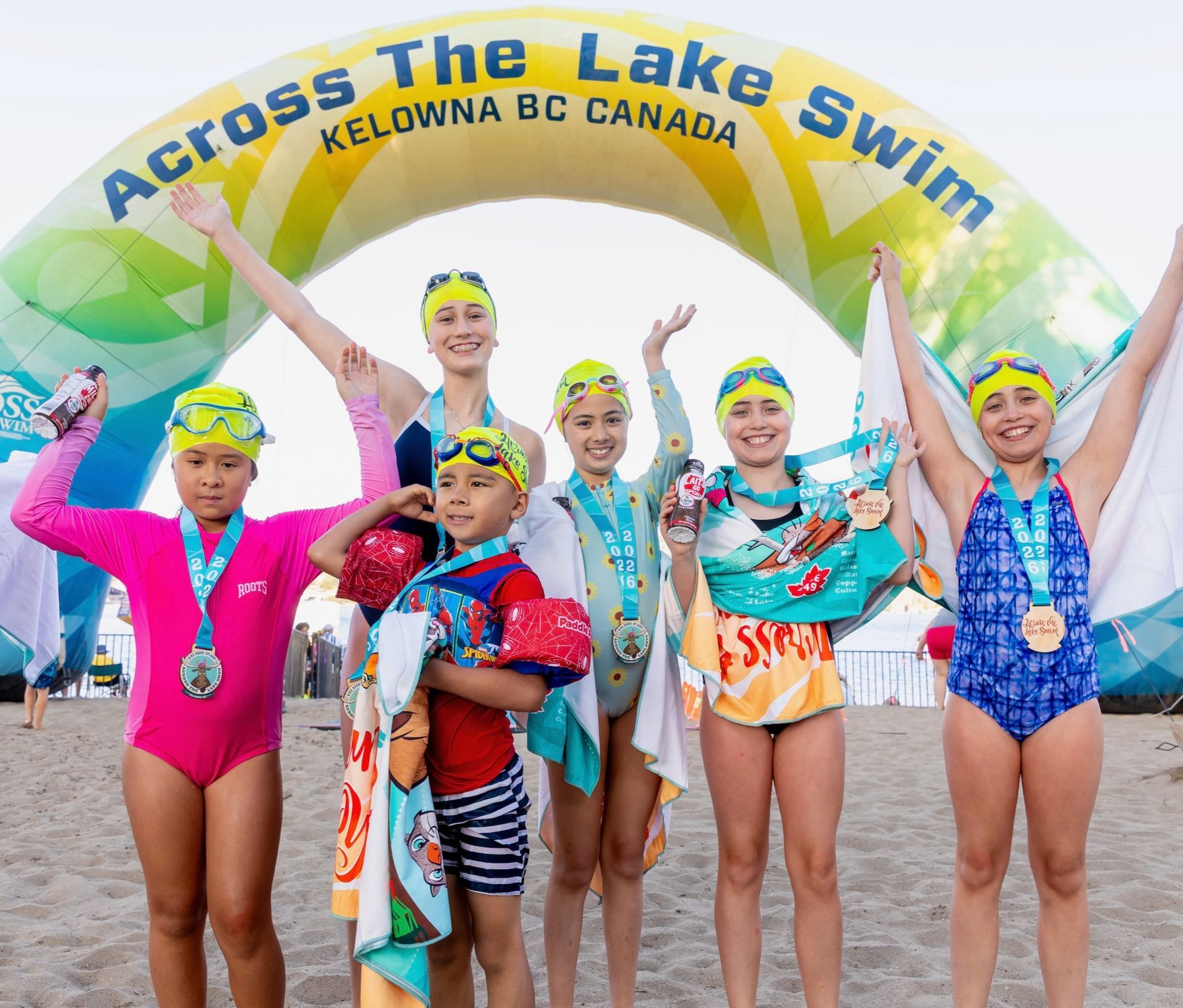 Kids Shore Splash swimmers with 2026 medals under the Across the Lake Swim arch in Kelowna