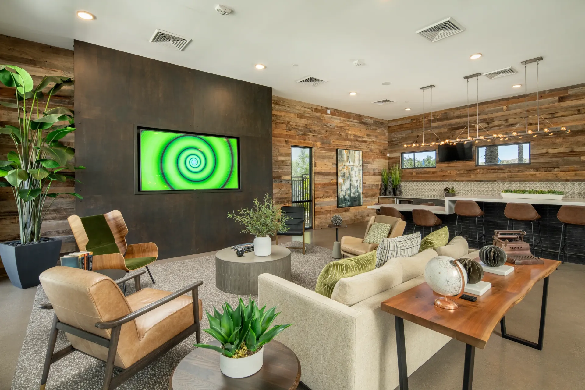 Modern lounge area with comfortable seating, a large television displaying a green spiral, and a bar with stools at Parc South Mountain in Phoenix, AZ.