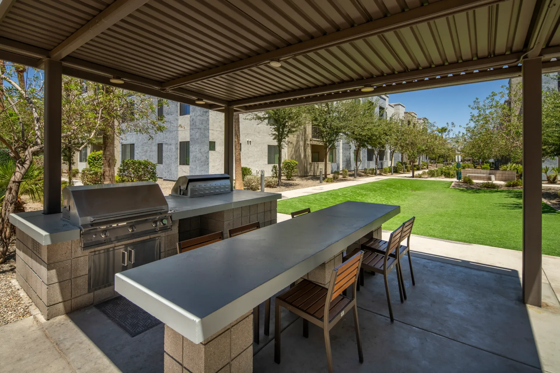 Outdoor kitchen with grills and a long counter with bar stools next to a grassy courtyard at Parc South Mountain in Phoenix, AZ.