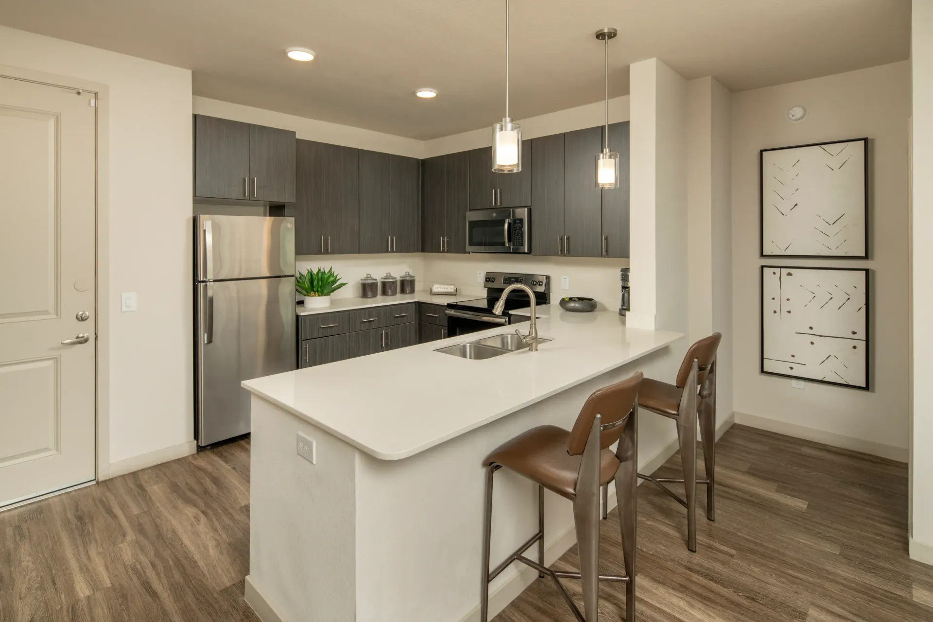 Modern kitchen with stainless steel appliances, dark grey cabinets, and a white quartz island with bar stools at Parc South Mountain in Phoenix, AZ.