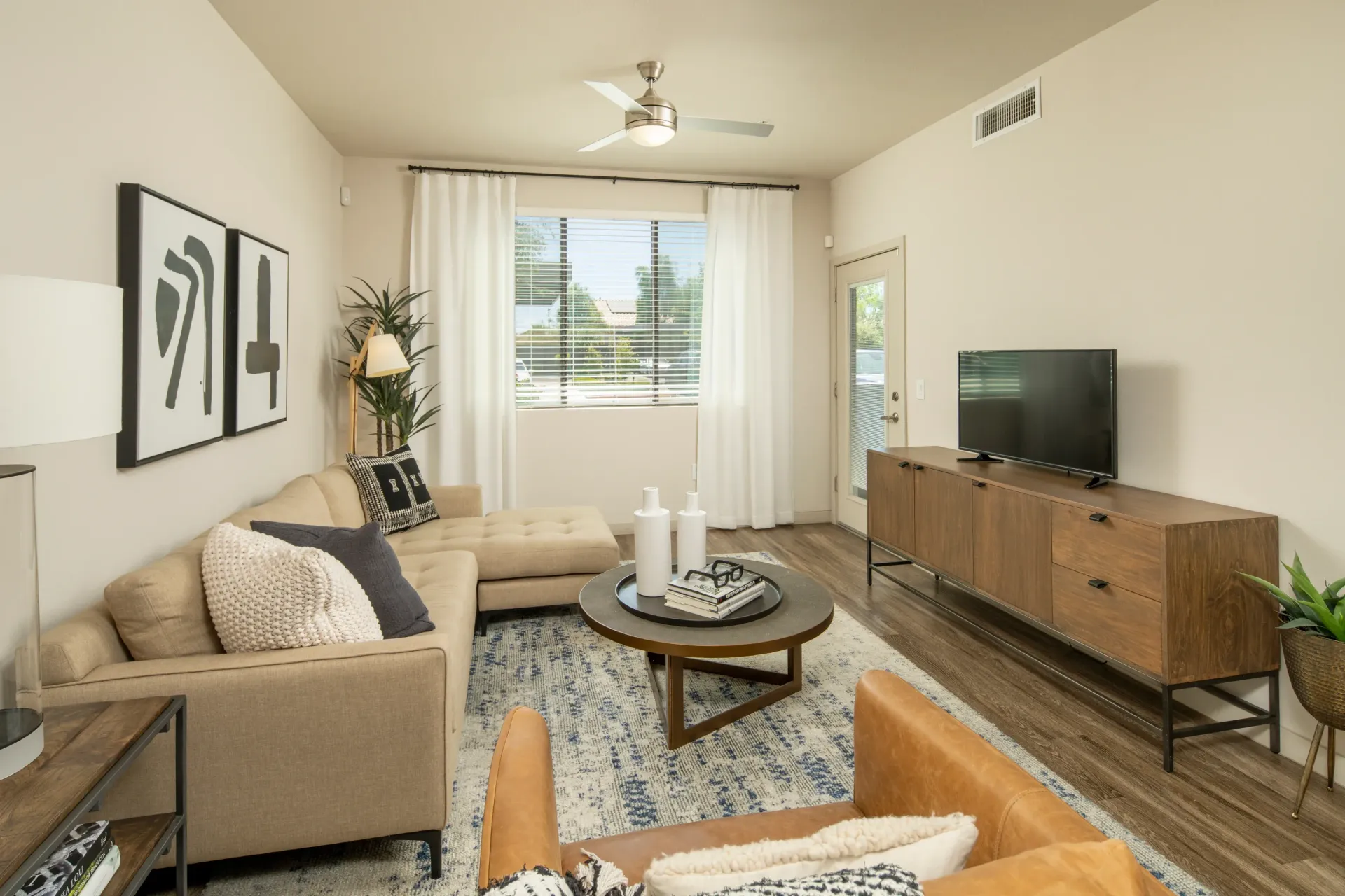 Modern living room with a sectional sofa, leather armchair, coffee table, and TV at Parc South Mountain in Phoenix, AZ.