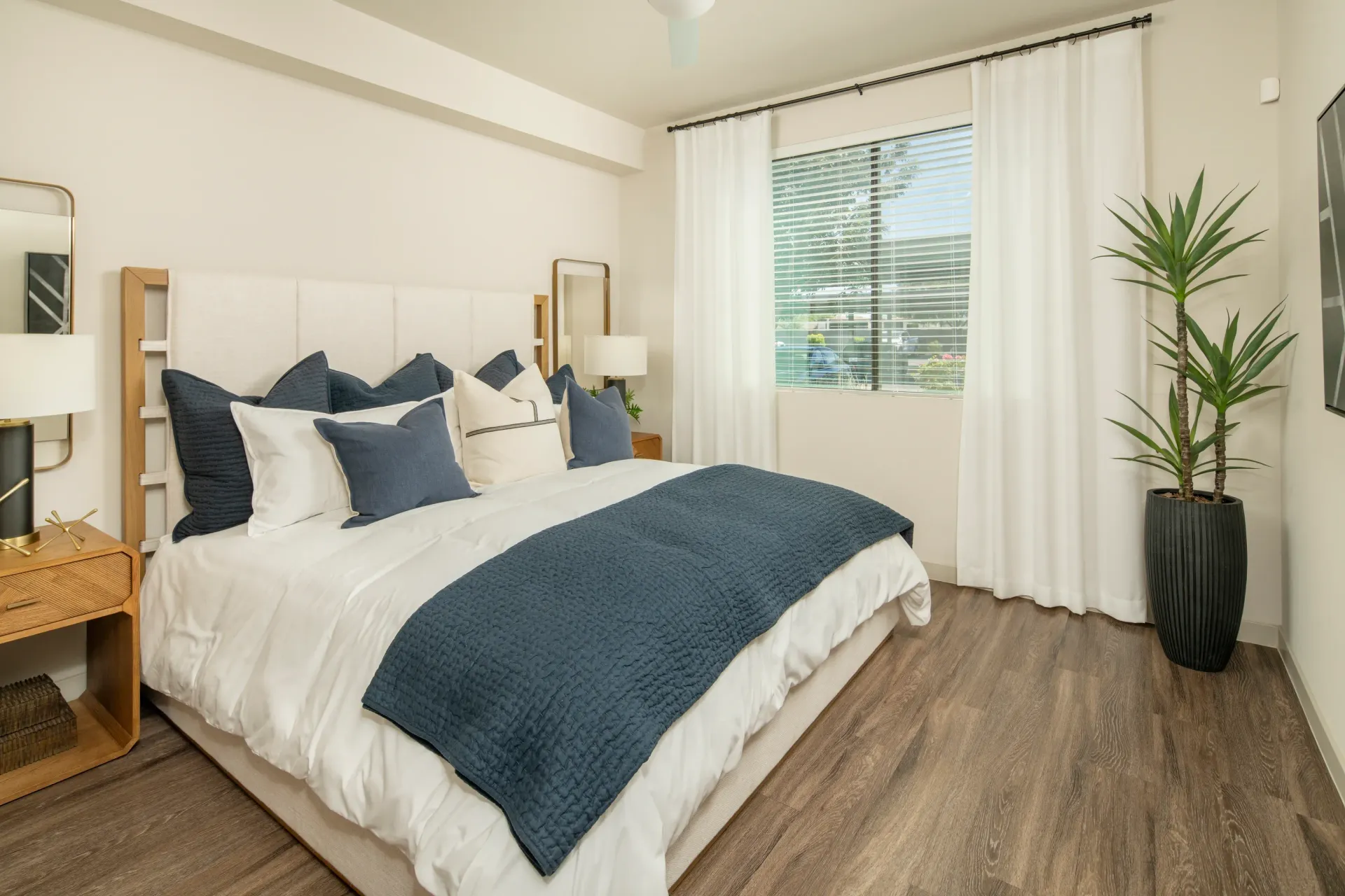 Modern bedroom with a king-size bed, navy and white bedding, nightstand, and large window with white curtains at Parc South Mountain in Phoenix, AZ.
