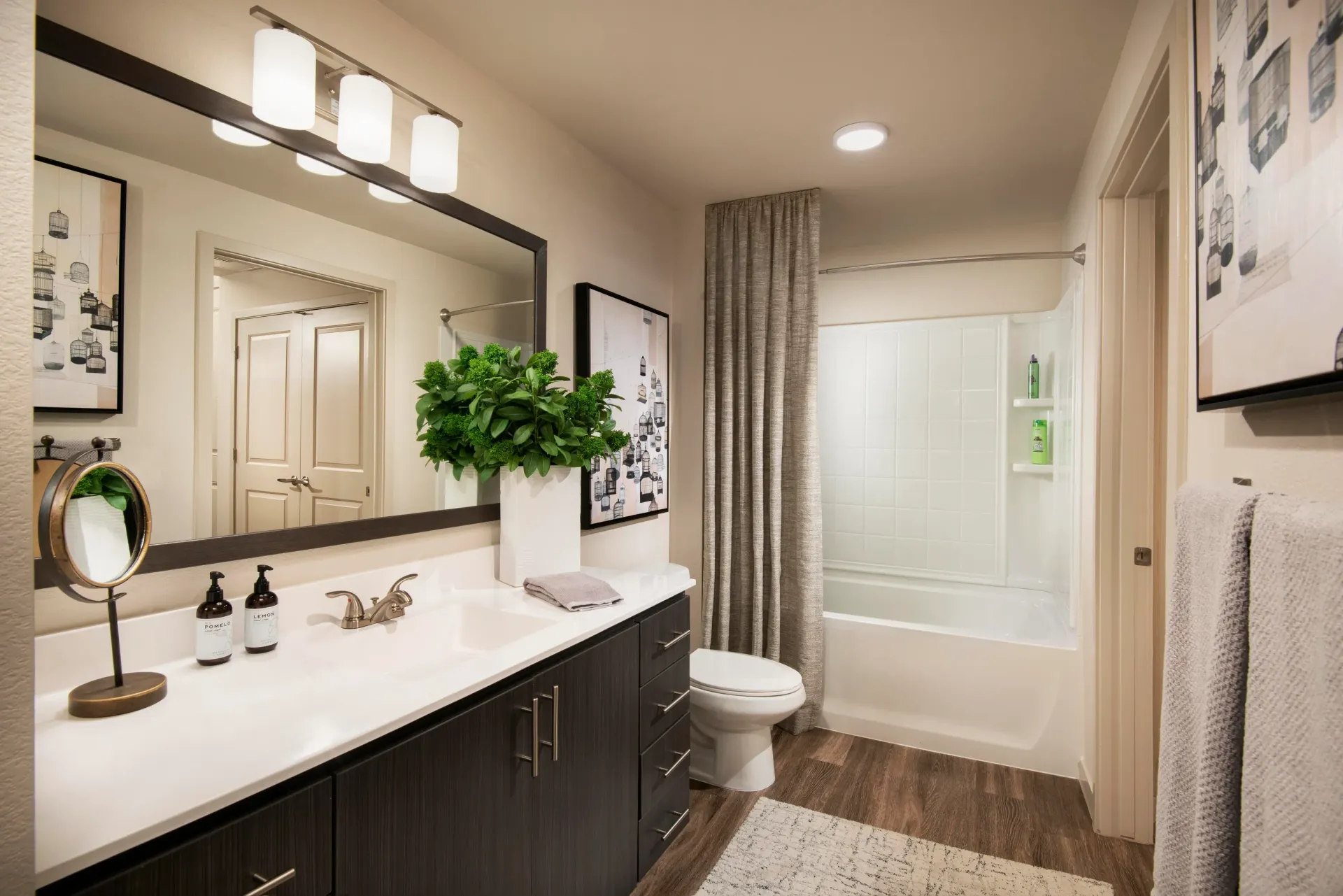 Modern bathroom with dark wood vanity, white countertop, large mirror, and a bathtub with shower at Parc South Mountain in Phoenix, AZ.