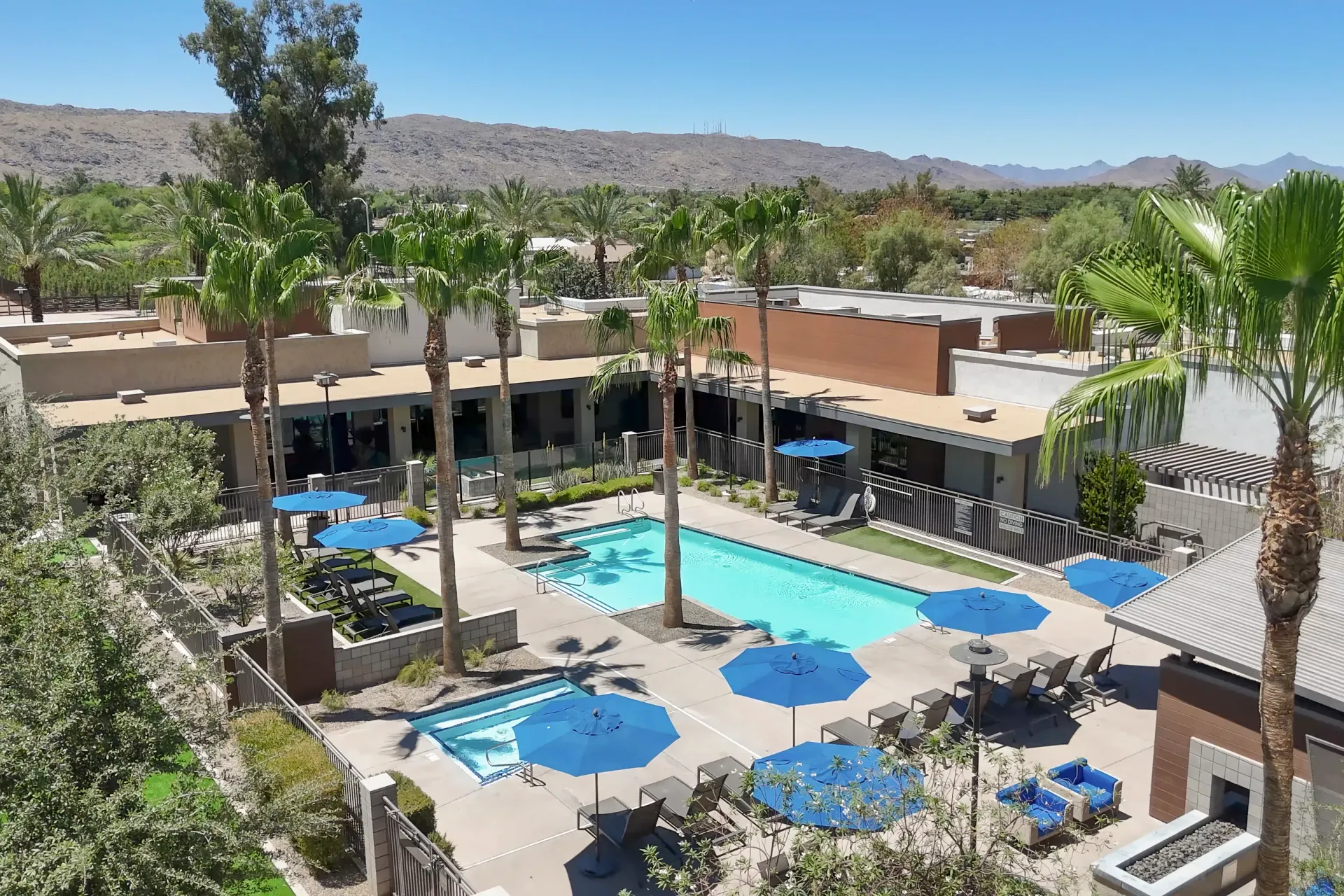 Aerial view of an outdoor swimming pool and hot tub area with lounge chairs and umbrellas.