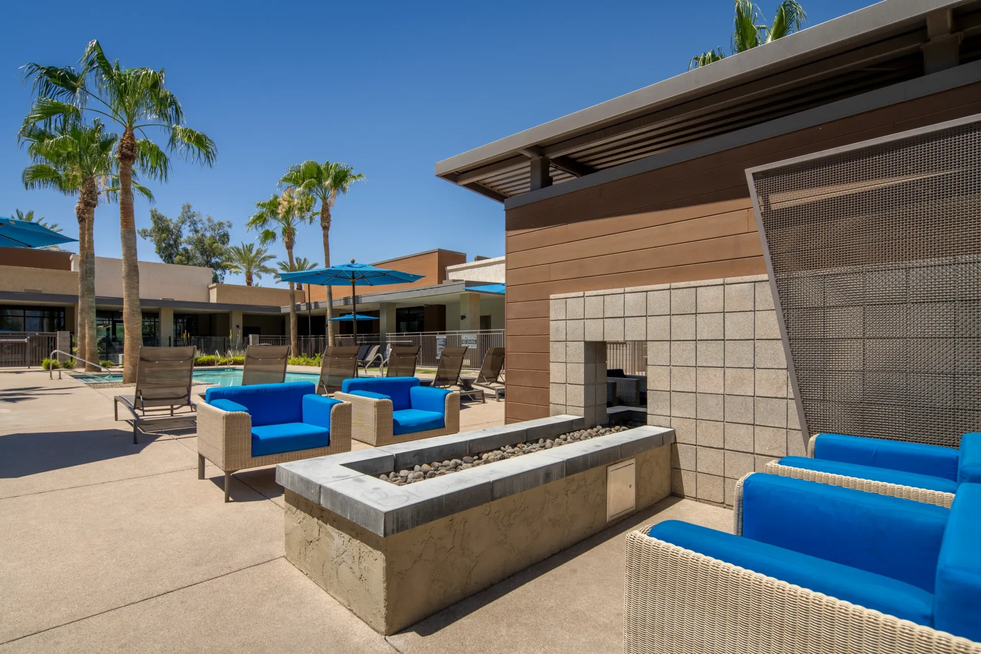 Outdoor pool area with lounge chairs, blue cushioned seating, and a modern gas fire pit at Parc South Mountain in Phoenix, AZ.