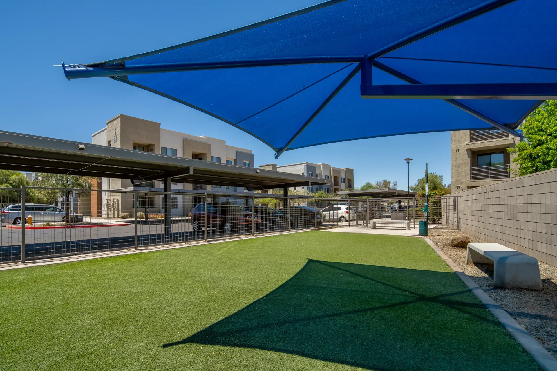 Dog park with artificial turf, shaded seating area, and covered parking at Parc South Mountain in Phoenix, AZ.