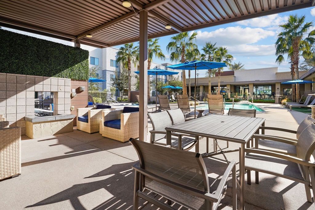 Outdoor community pool area with covered seating, lounge chairs, and blue umbrellas at Parc South Mountain in Phoenix, AZ.