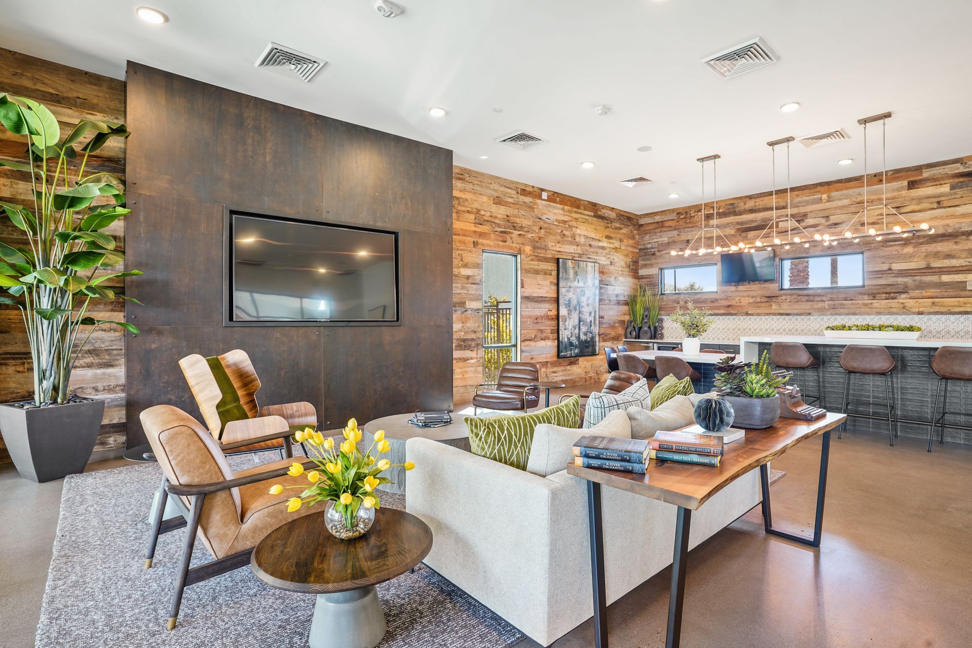 Cozy lounge with wood paneling, TV, seating areas, plants, and a long bar at Parc South Mountain in Phoenix, AZ..
