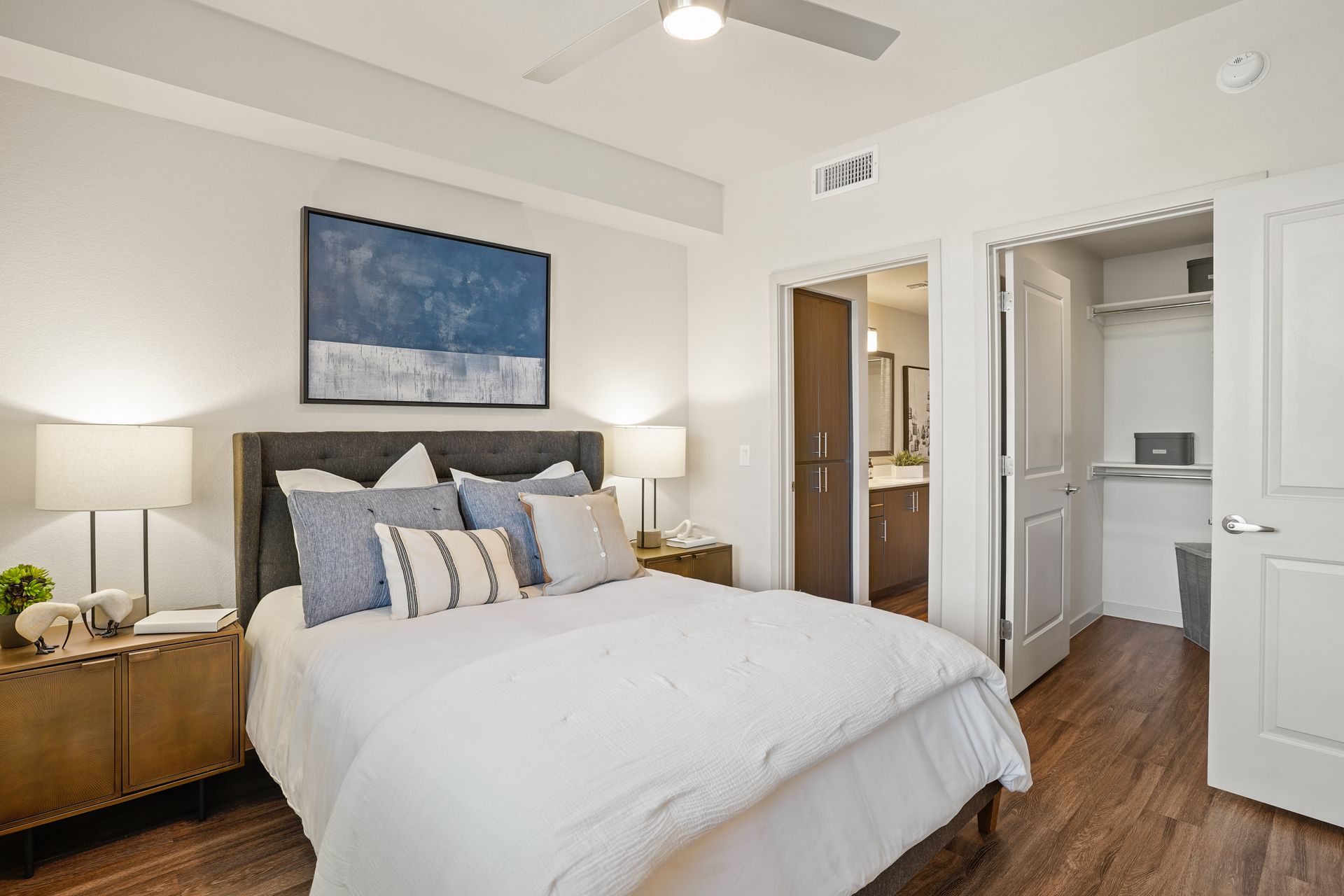 Bedroom with bed, closet, and bathroom door; neutral tones, modern design, artwork at Parc South Mountain in Phoenix, AZ..