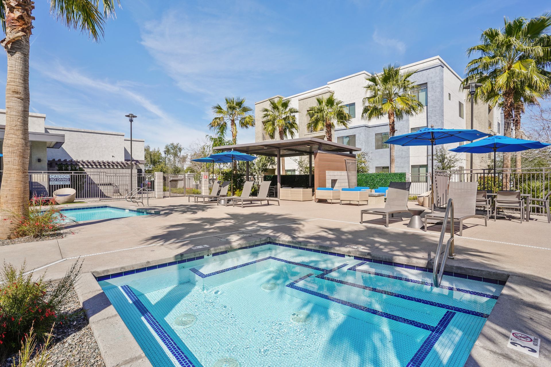 Pool area with jacuzzi, lounge chairs, umbrellas, and multi-story building at Parc South Mountain in Phoenix, AZ..