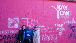 A group of people are standing in front of a pink wall.