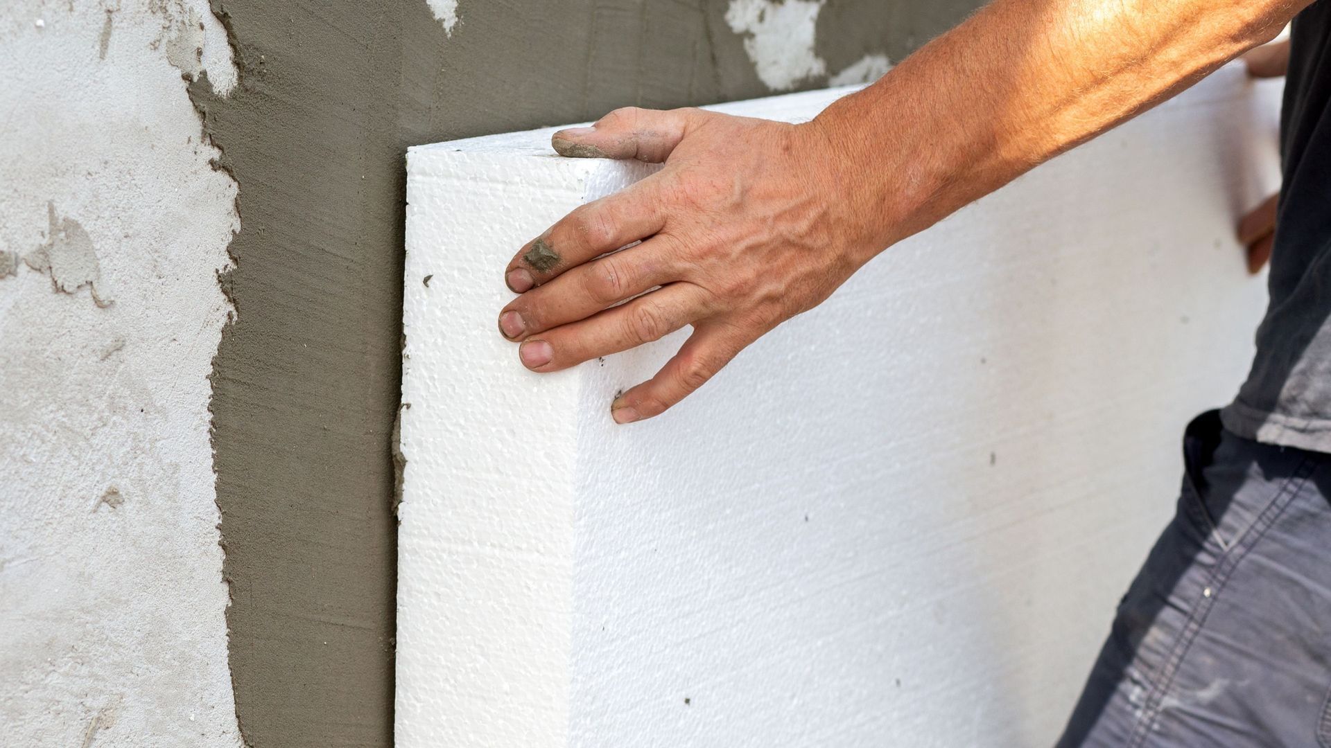 A man is holding a piece of styrofoam on a wall.