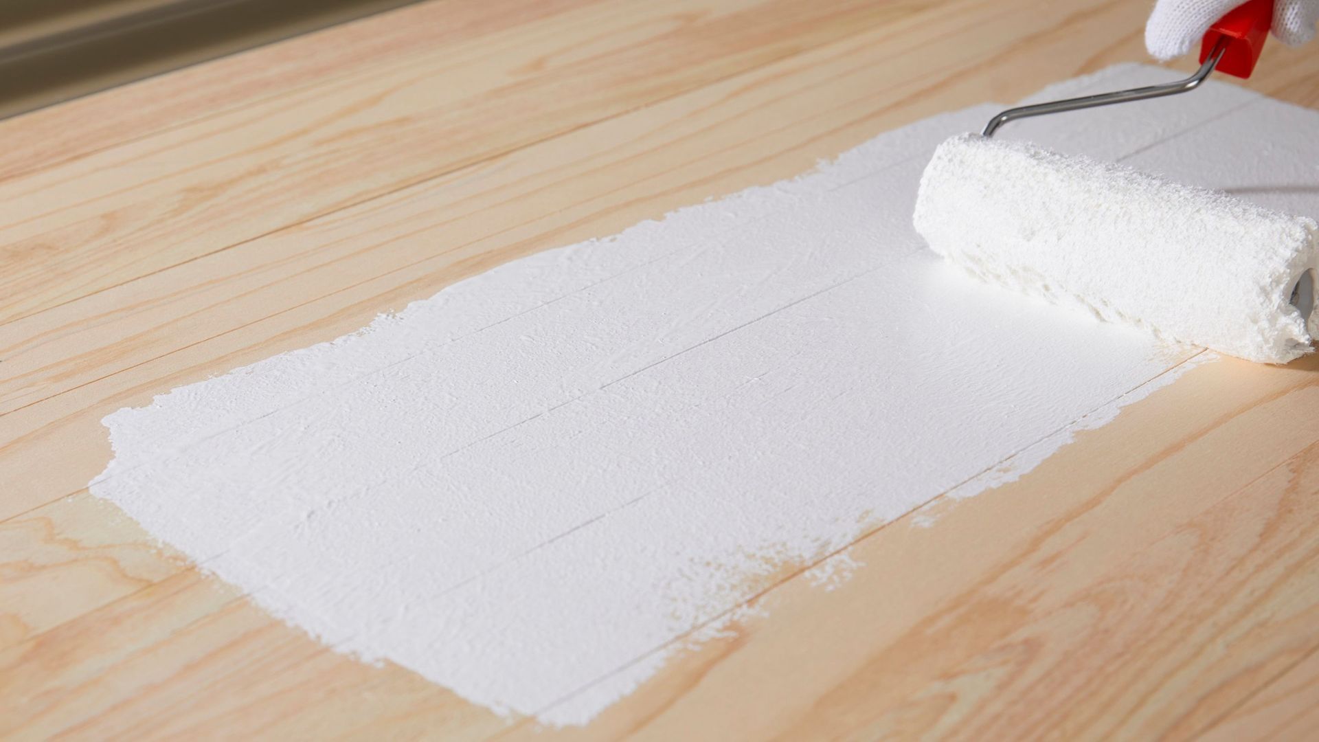 A person is painting a wooden surface with a paint roller.