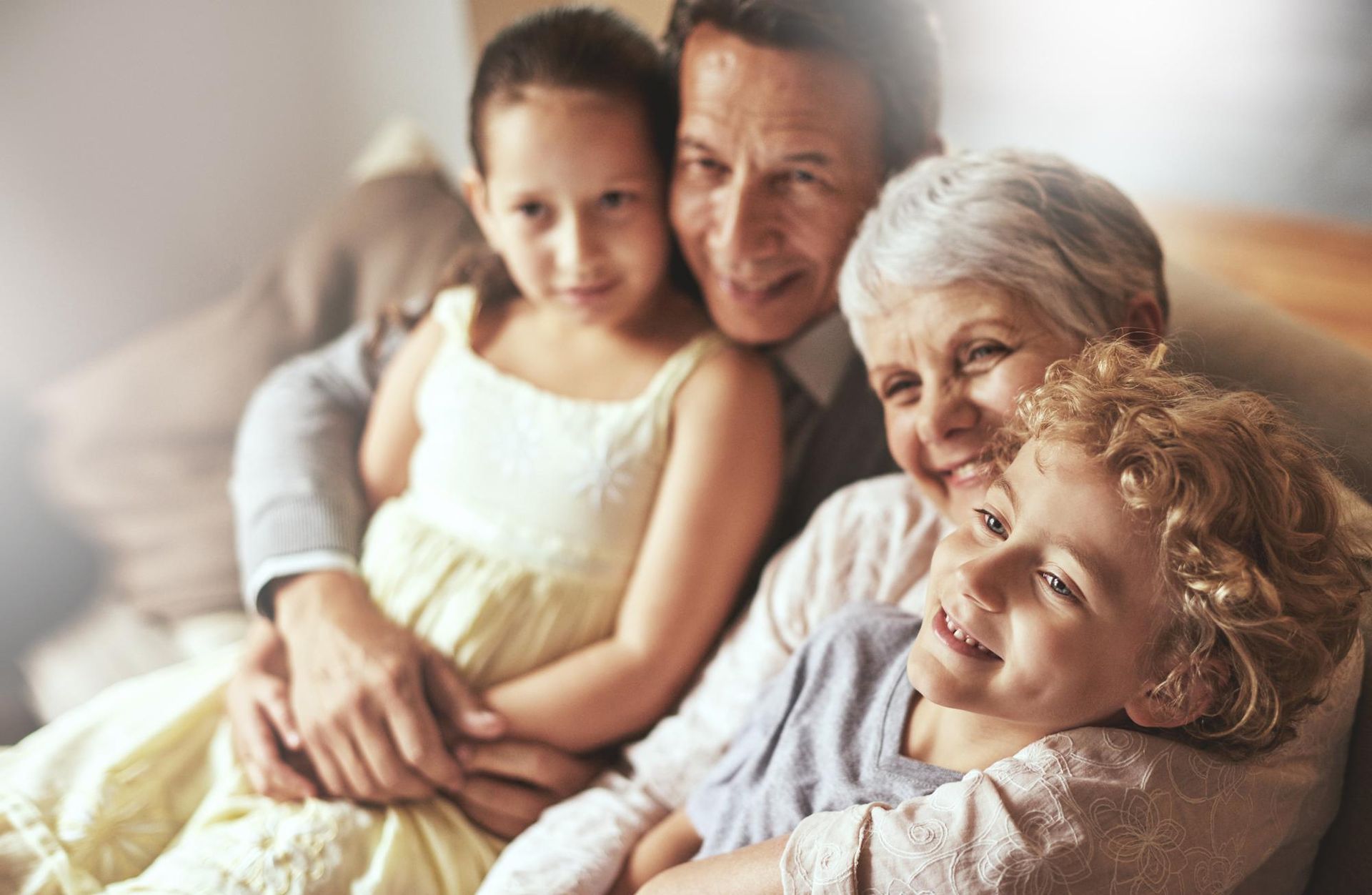 Grandparents embracing two grandchildren on a couch, smiling warmly indoors.